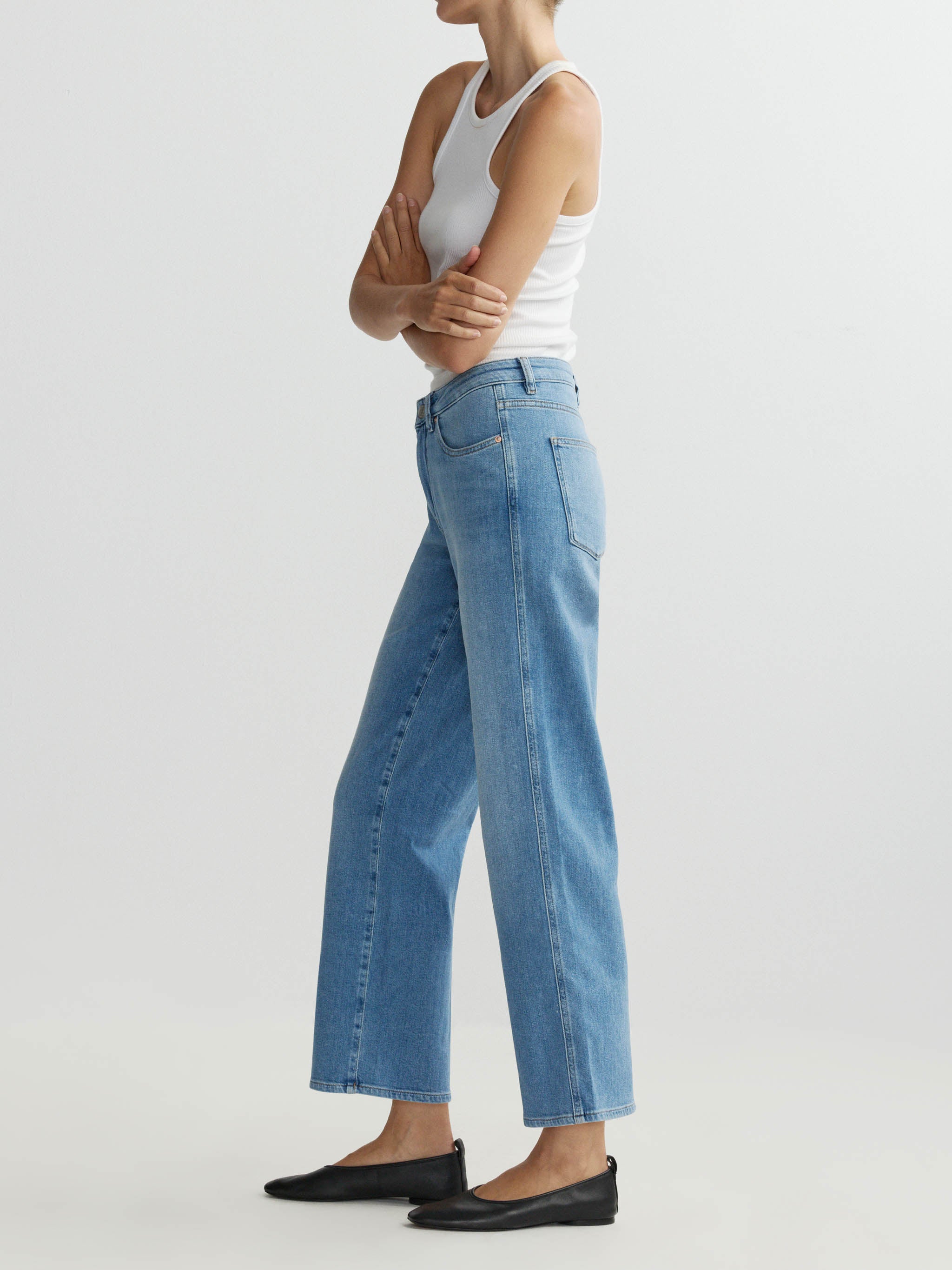Person wearing blue jeans and a white tank top on a light gray background