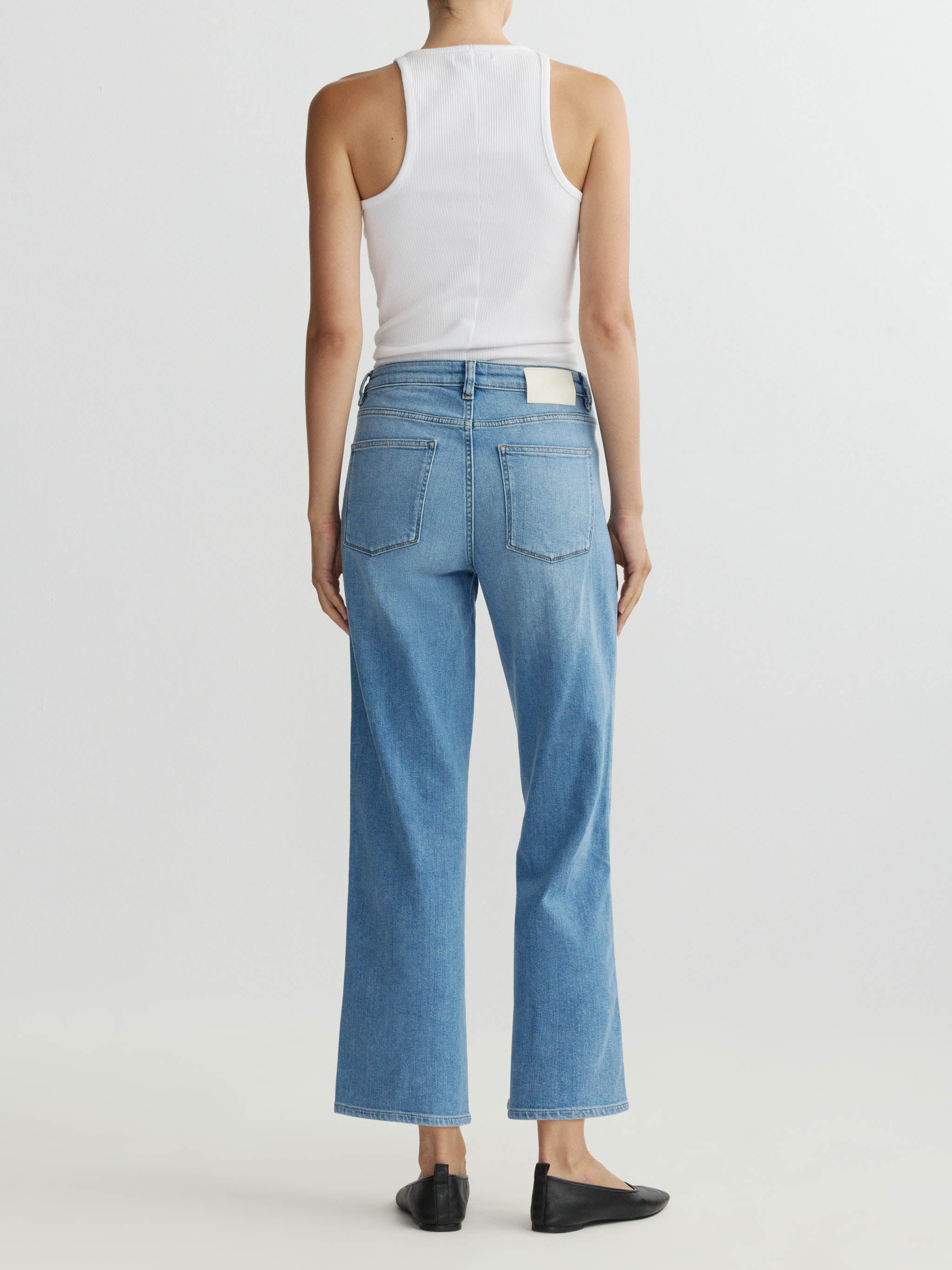 Person wearing a white tank top and blue jeans on a plain background