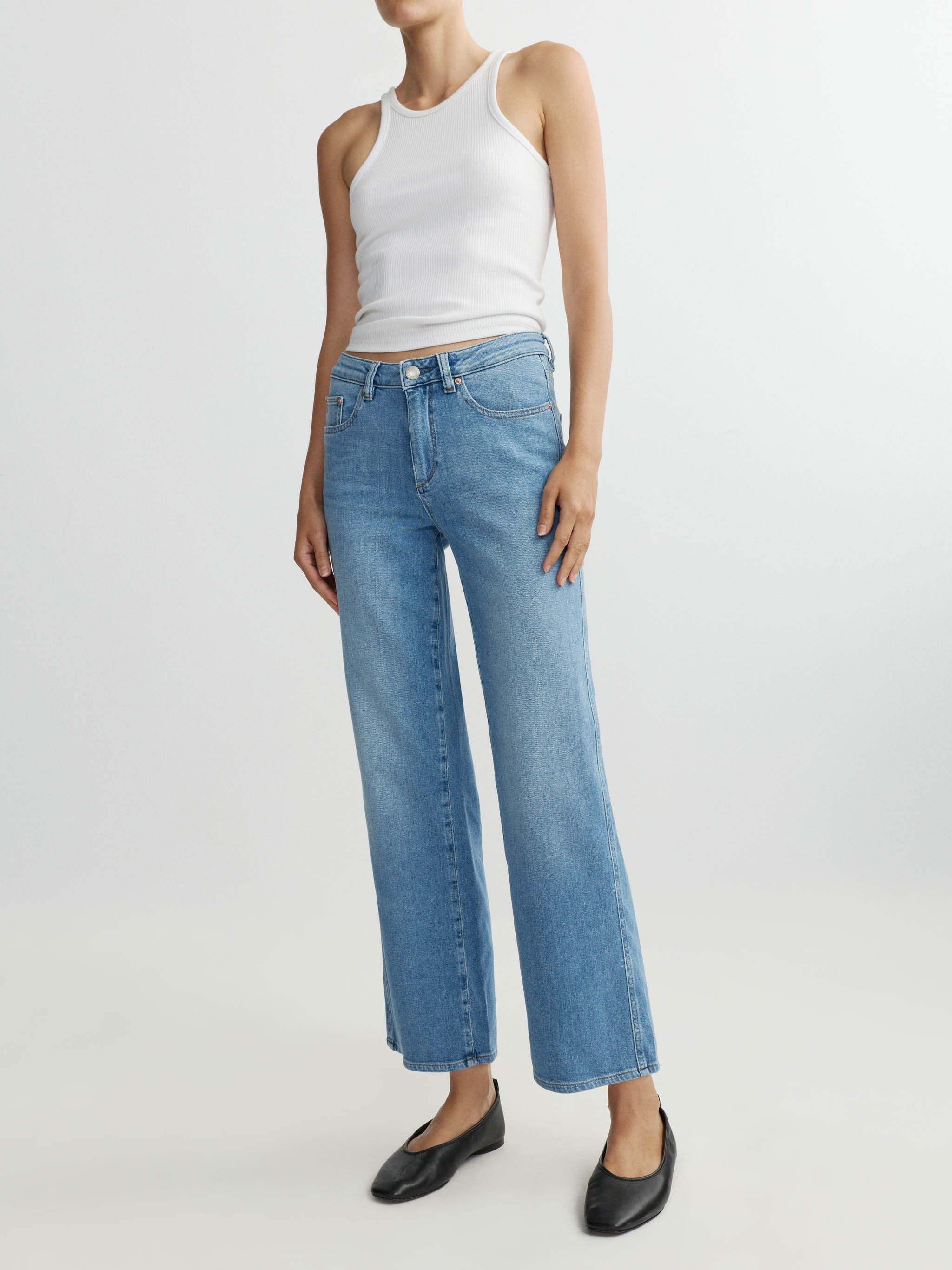 Person wearing a white tank top and blue jeans on a white background