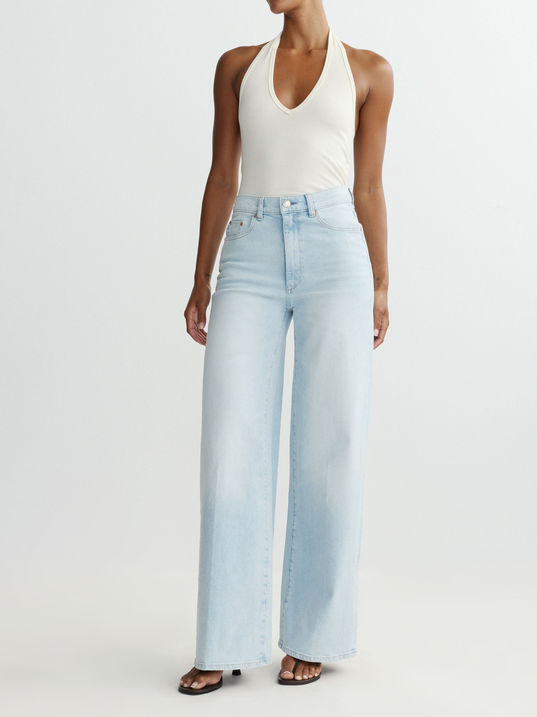 Person wearing light blue jeans and a white tank top on a white background