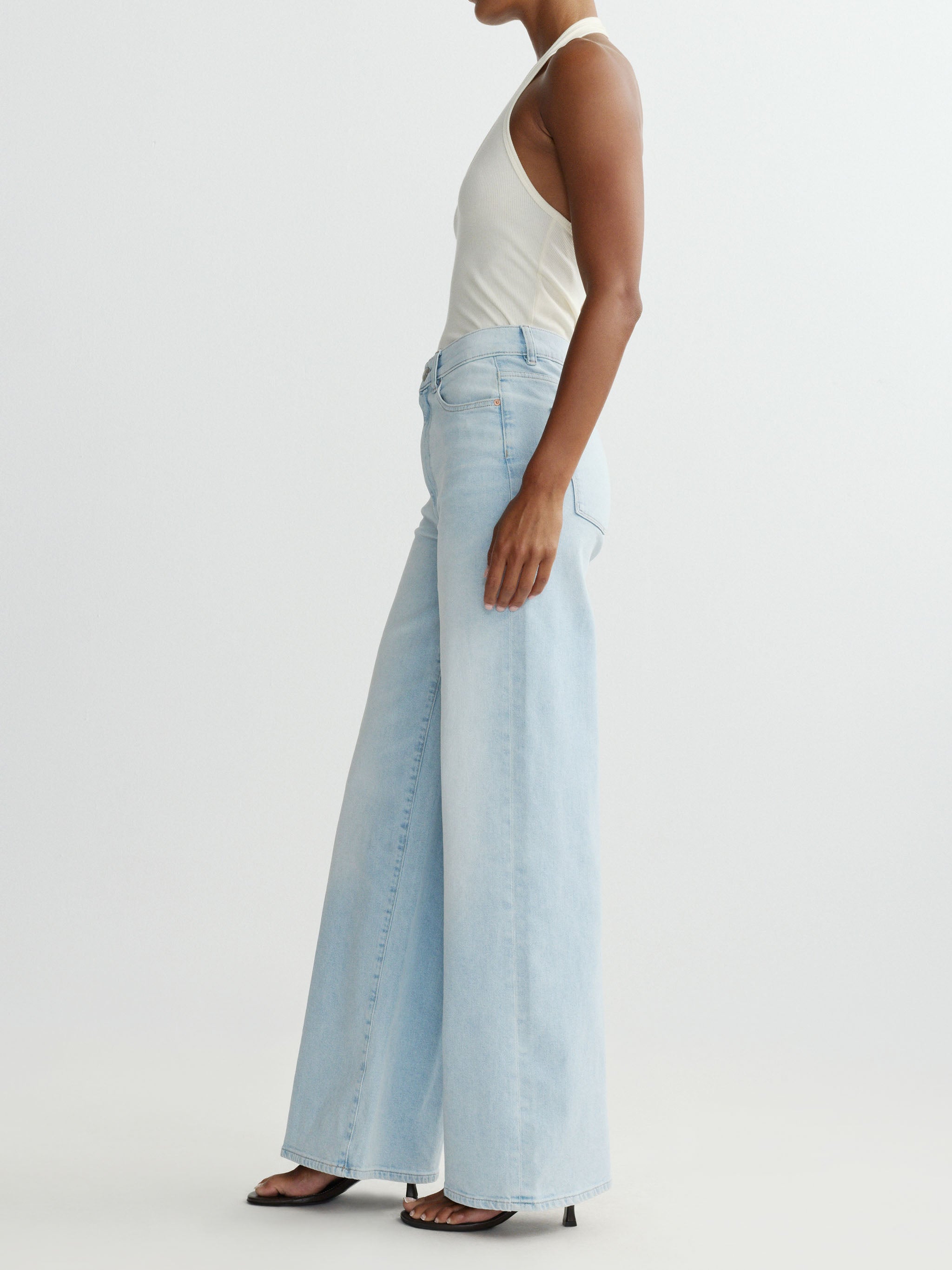 Woman wearing light blue jeans and a white top on a plain background