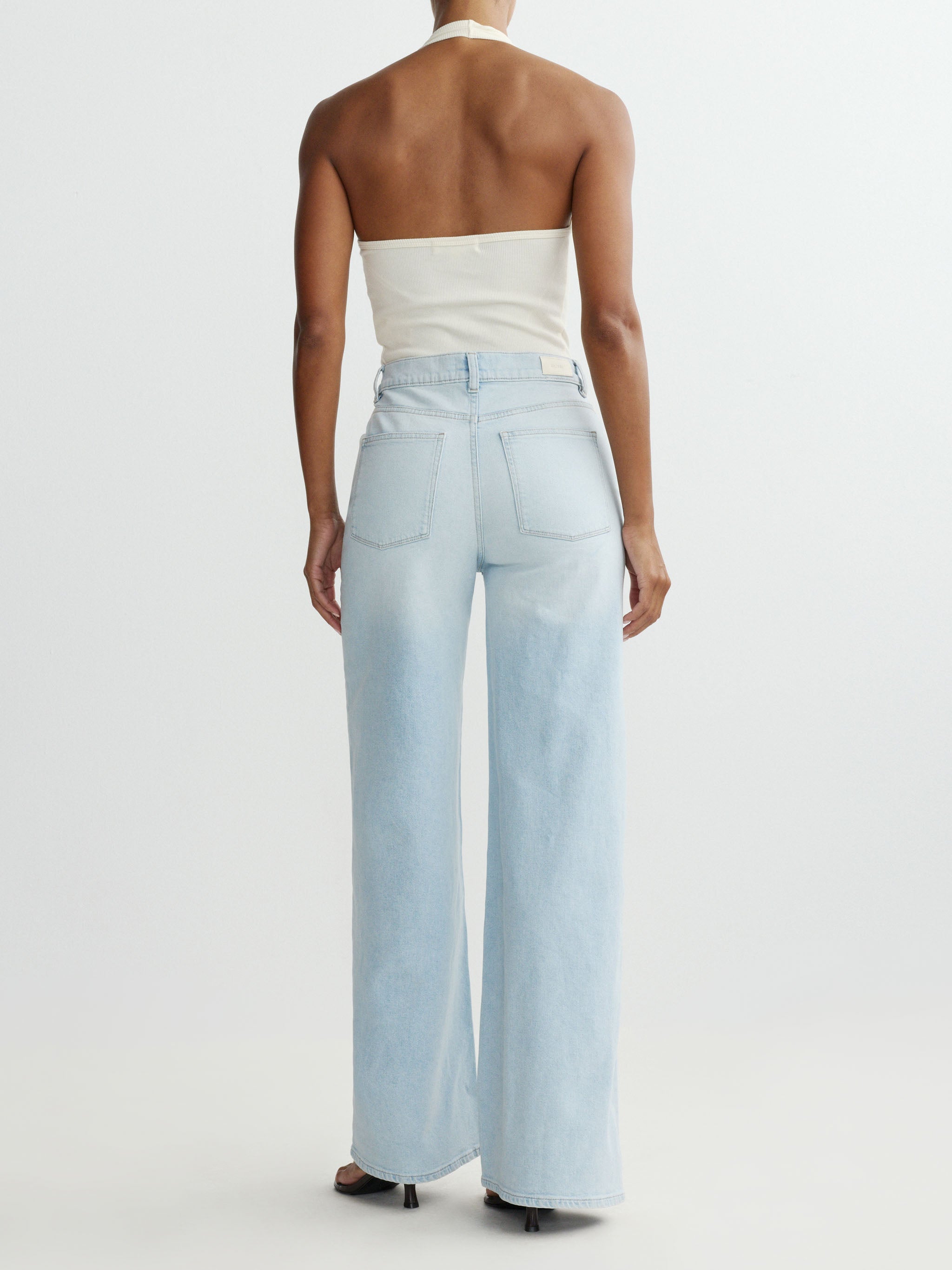 Person wearing light blue wide-leg jeans and a white strapless top on a plain background