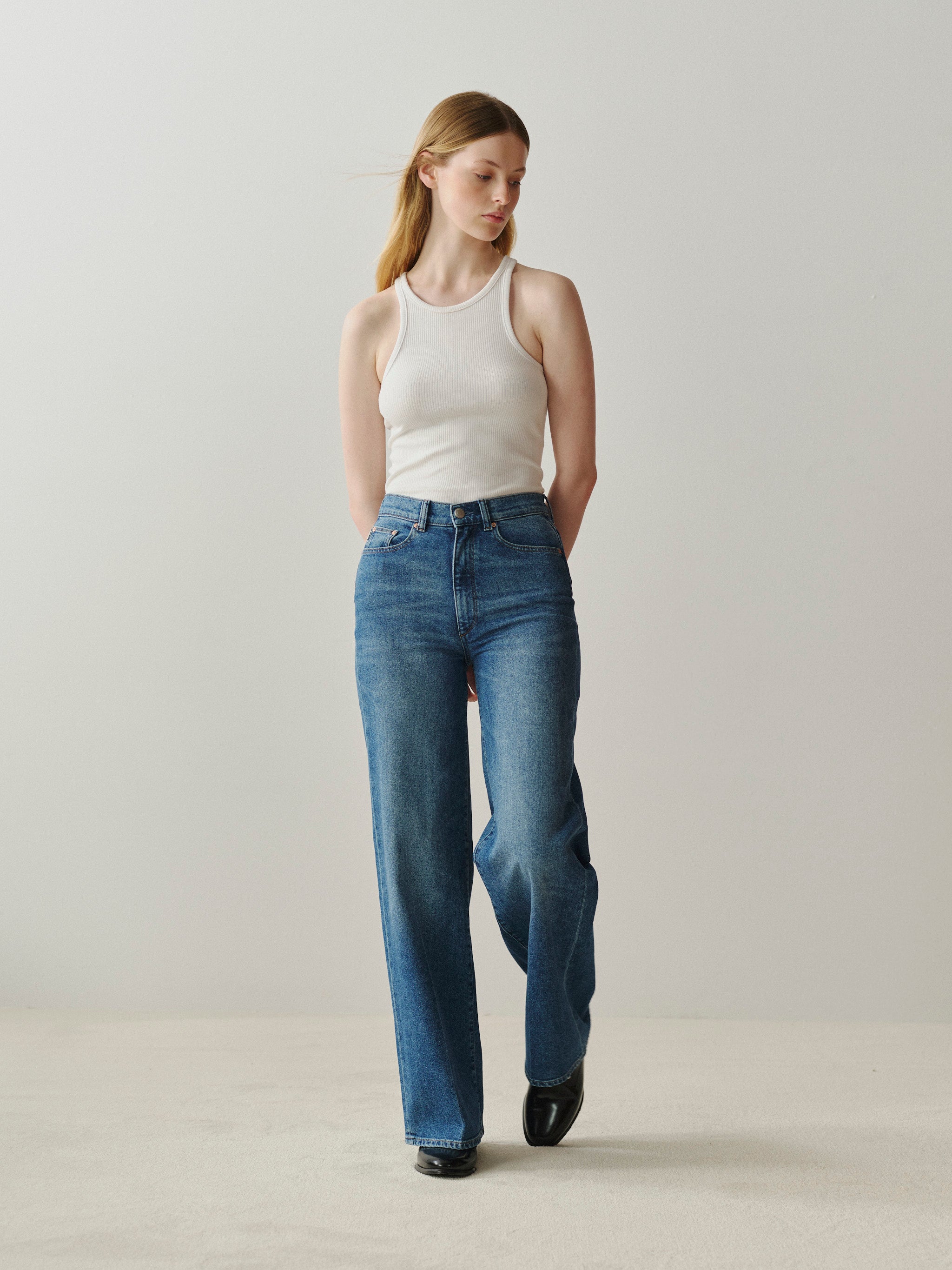 Woman wearing a white tank top and blue jeans against a plain background