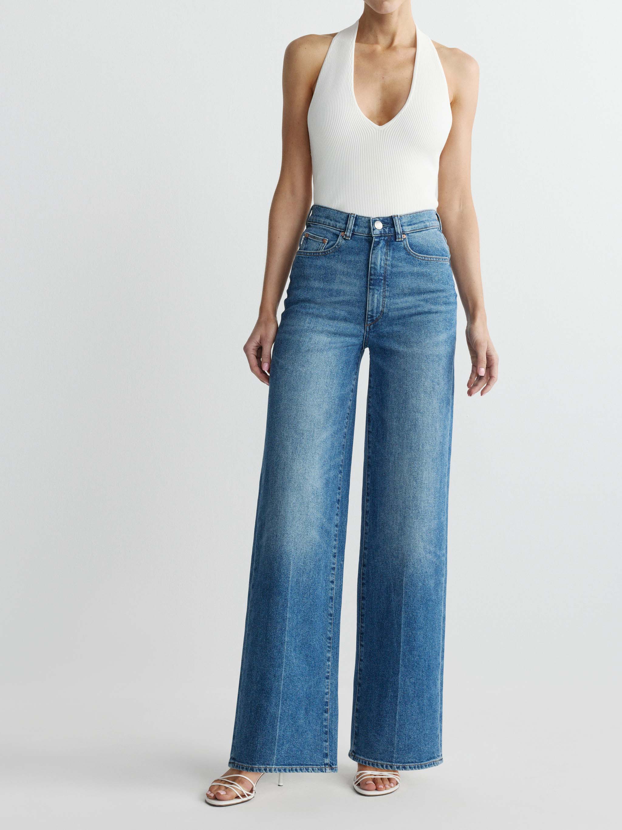 Person wearing a white tank top and blue jeans on a light gray background
