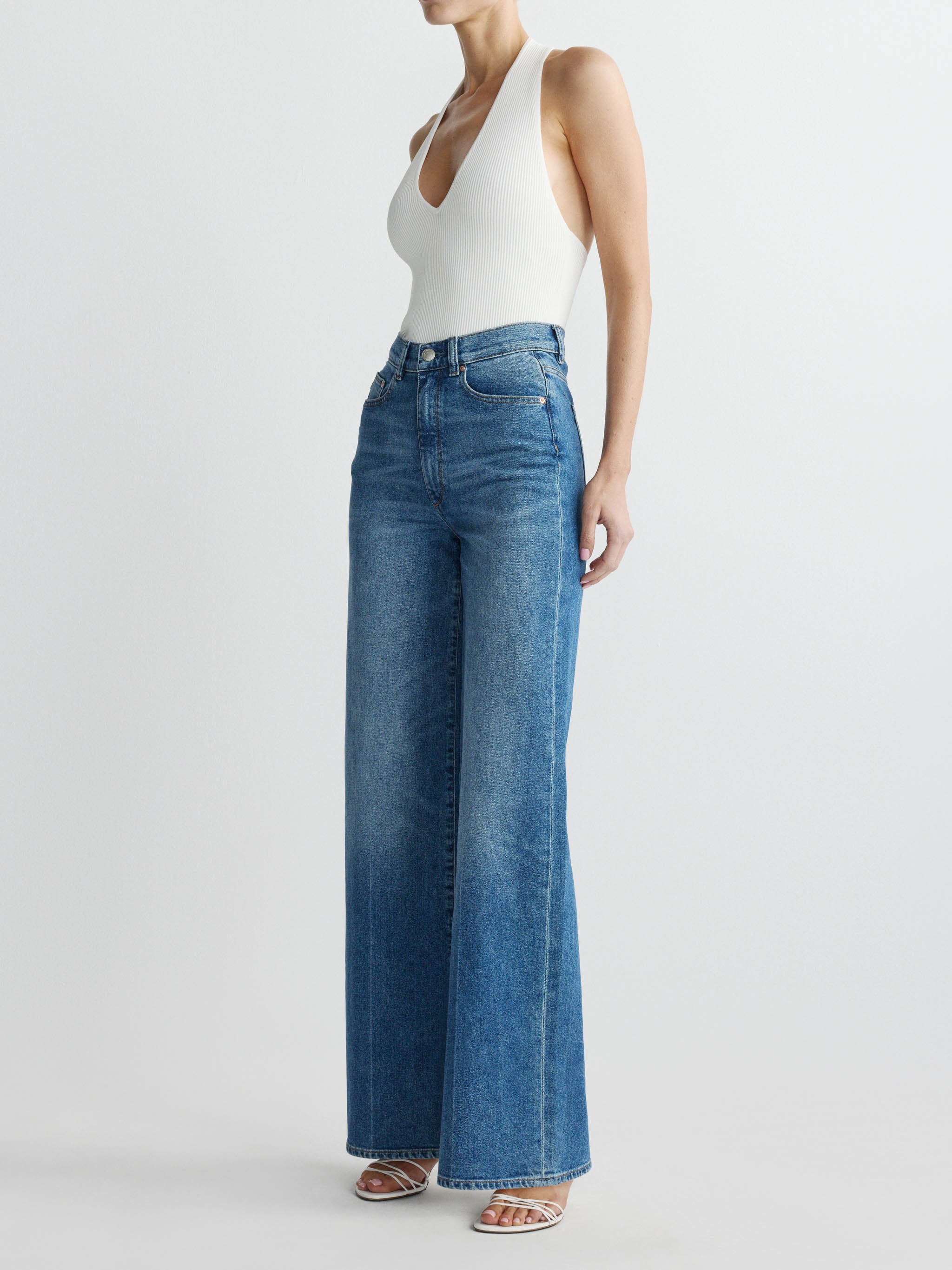 Person wearing blue jeans and a white top on a light gray background
