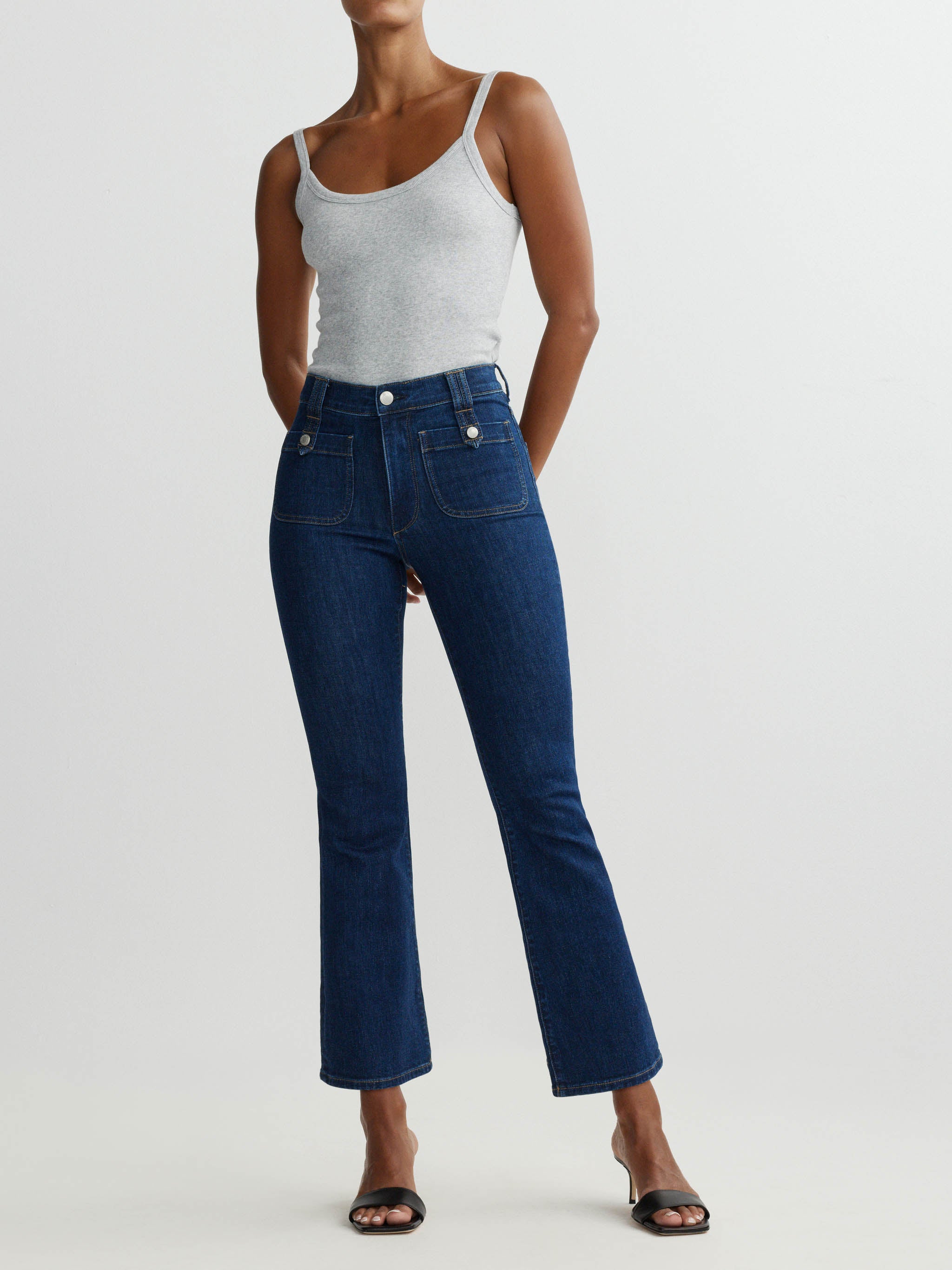 Person wearing a white tank top and blue jeans on a light gray background