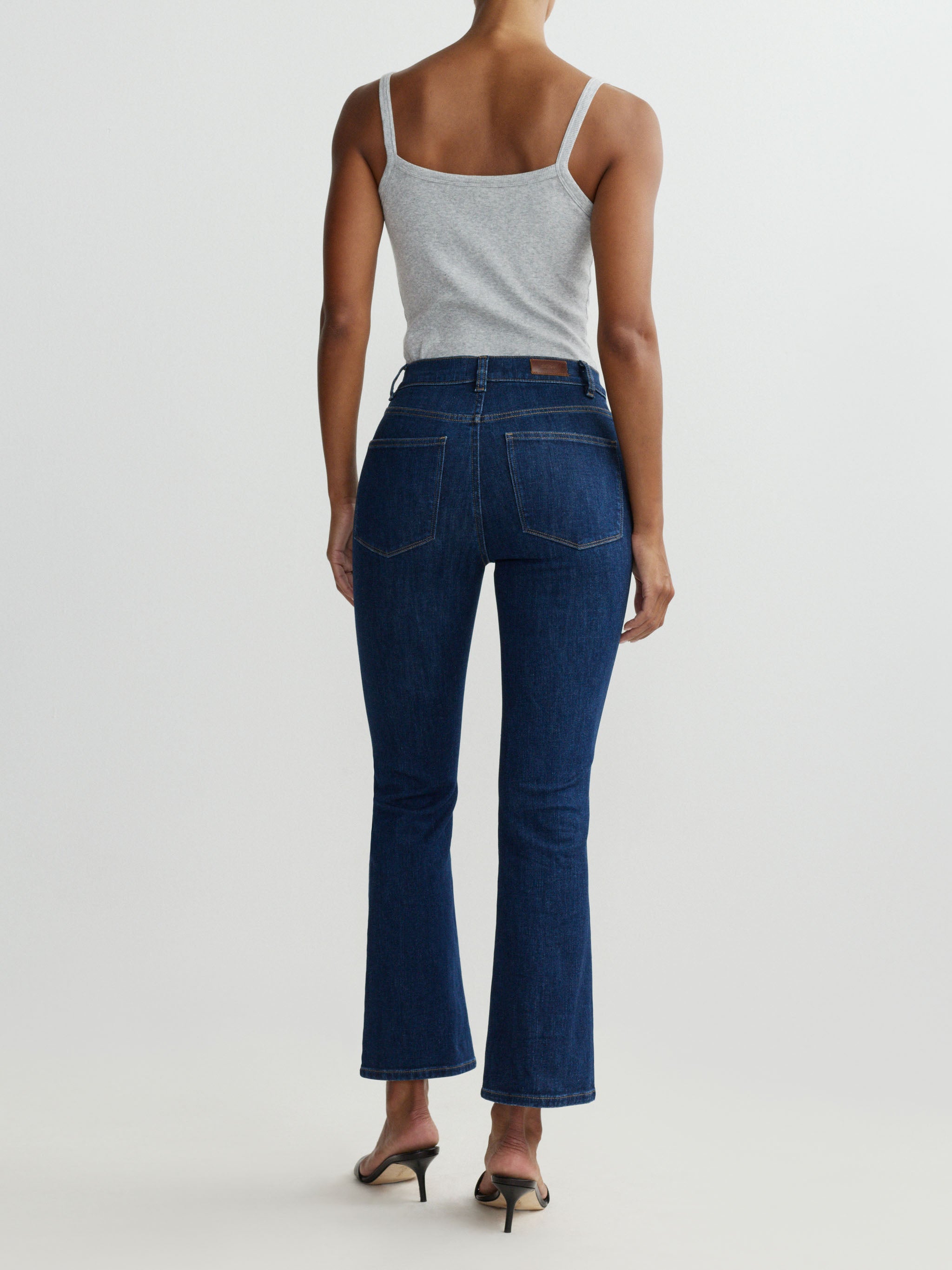 Person wearing blue jeans and a gray tank top on a white background