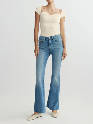 Person wearing a cream top and blue flared jeans on a white background