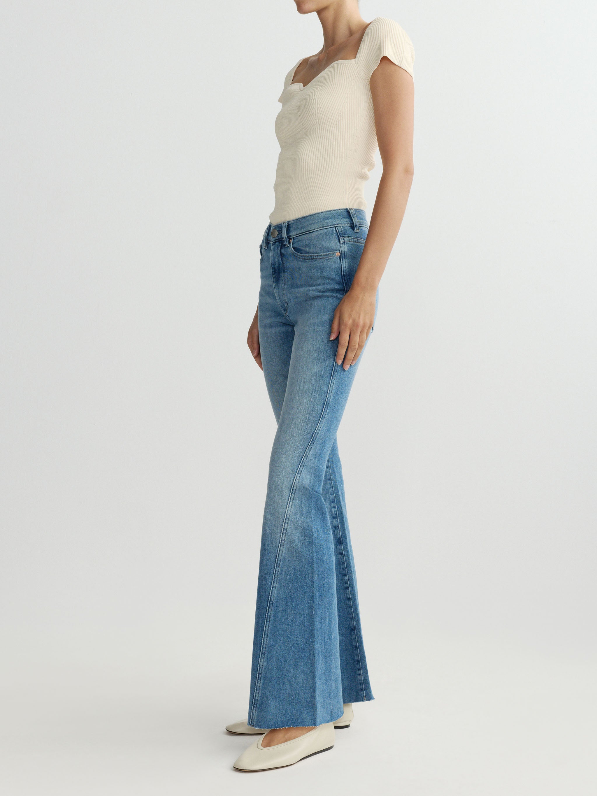 Woman wearing blue flared jeans and a white top on a light gray background
