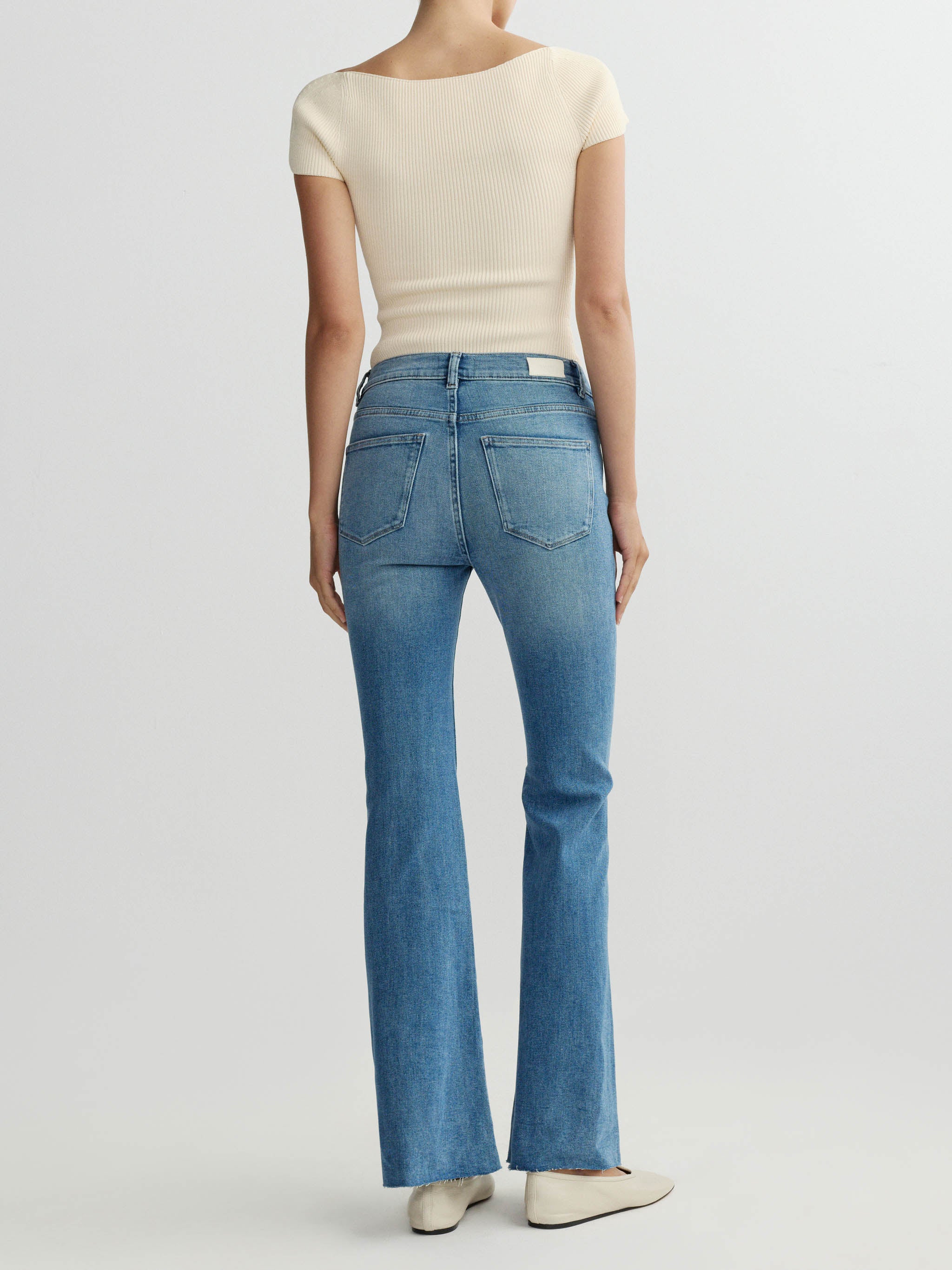 Person wearing blue jeans and a beige top on a white background