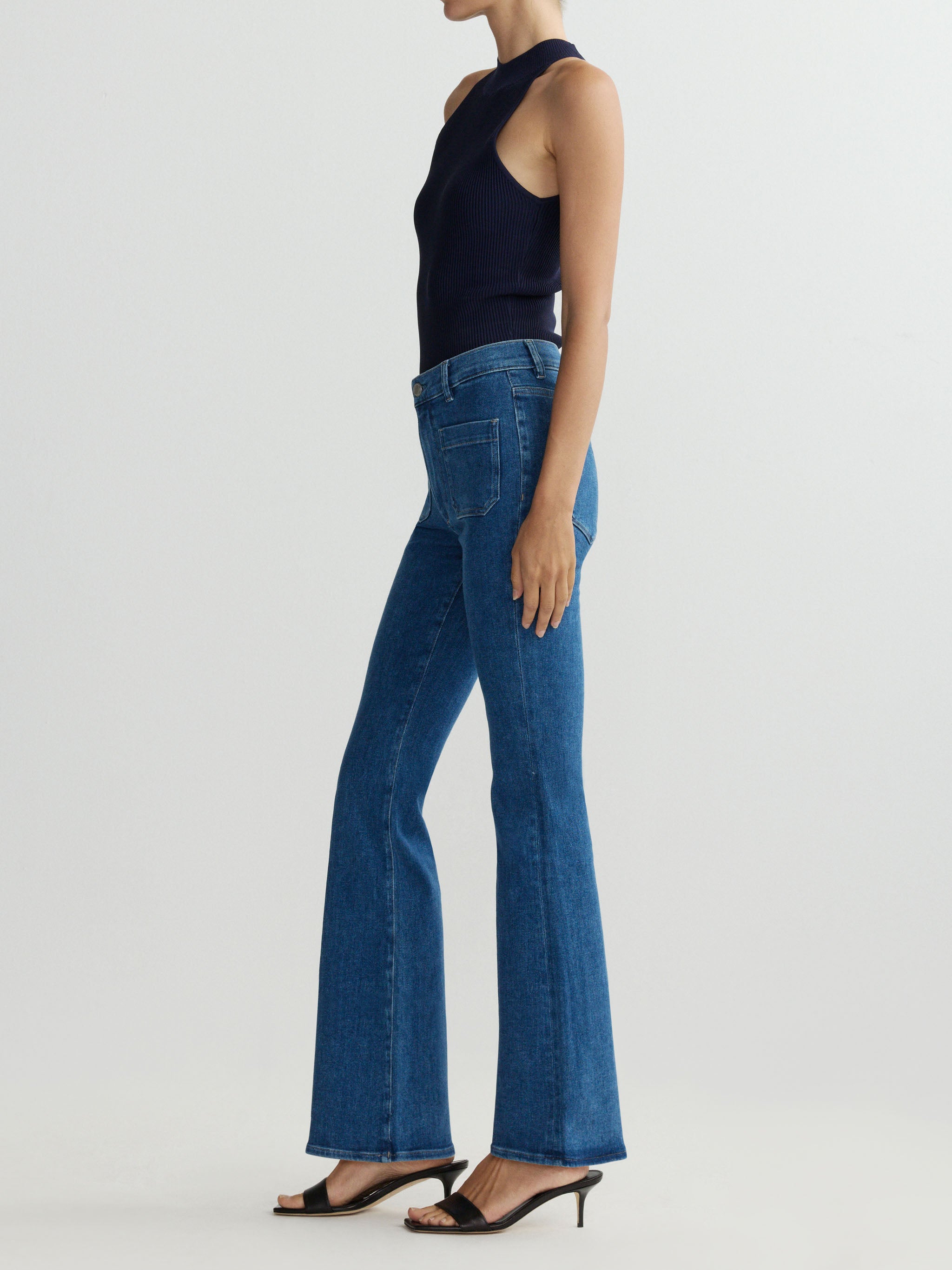 Person wearing blue jeans and a black sleeveless top on a white background