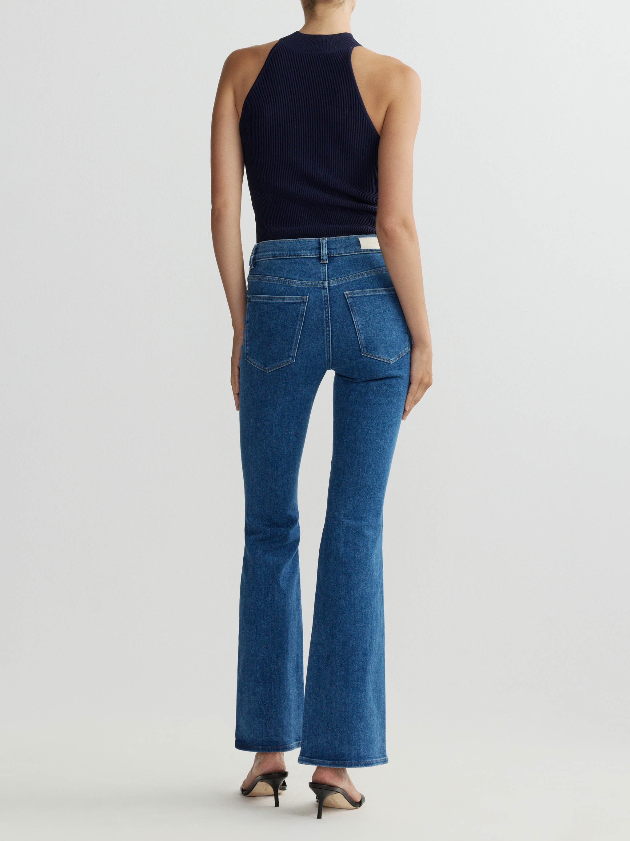 Person wearing blue jeans and a black top on a white background