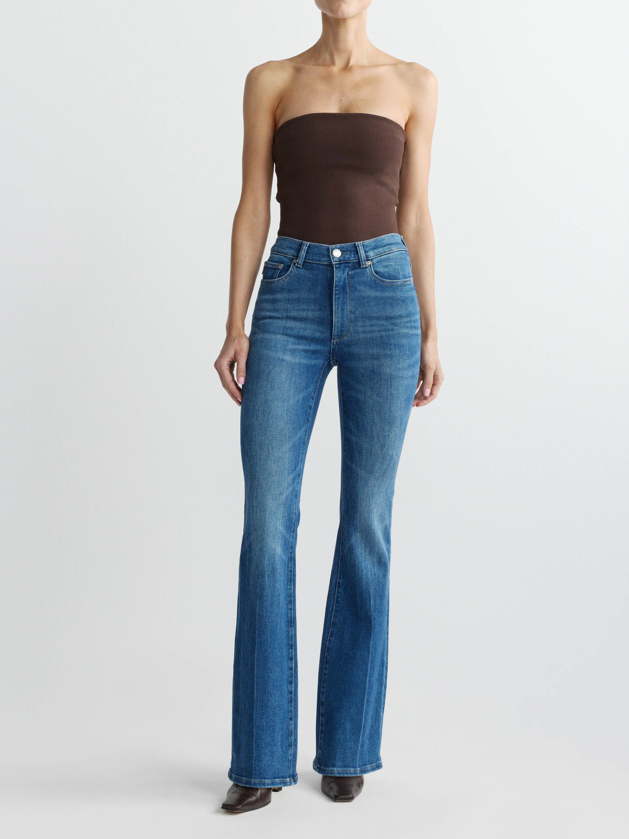 Person wearing blue flared jeans and a brown strapless top on a white background