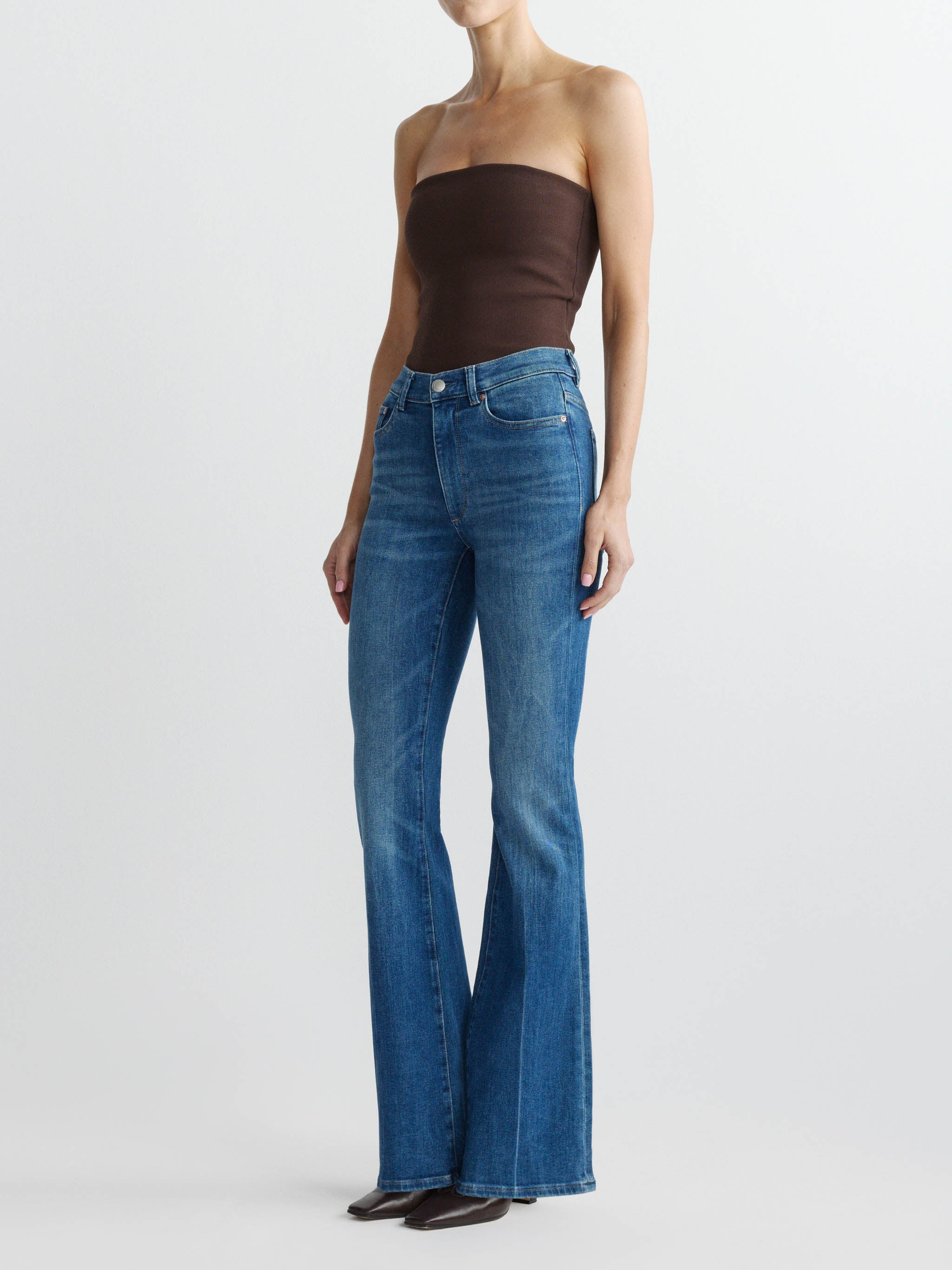 Person wearing blue flared jeans and a brown strapless top on a white background