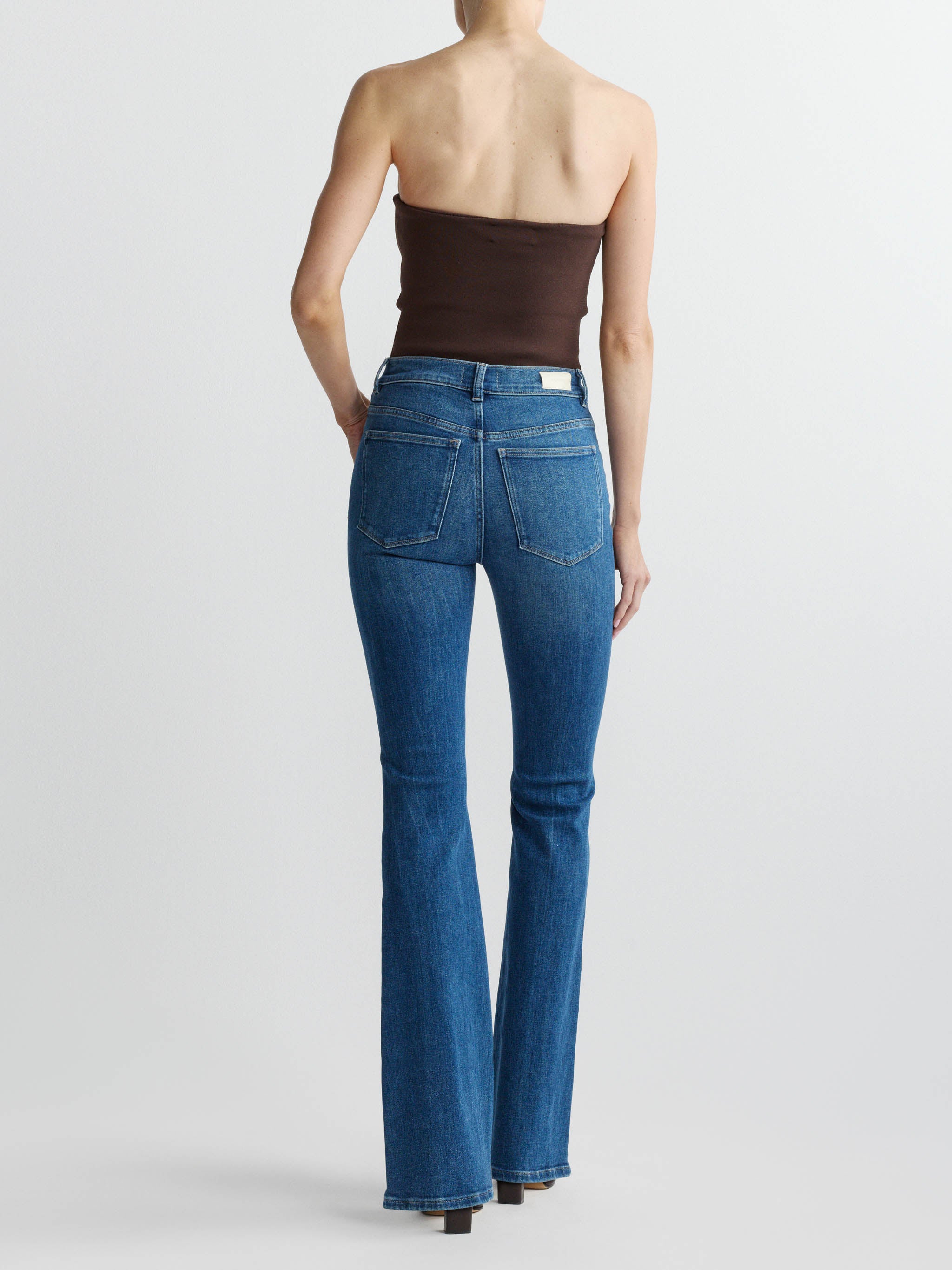 Person wearing blue jeans and a brown strapless top on a white background