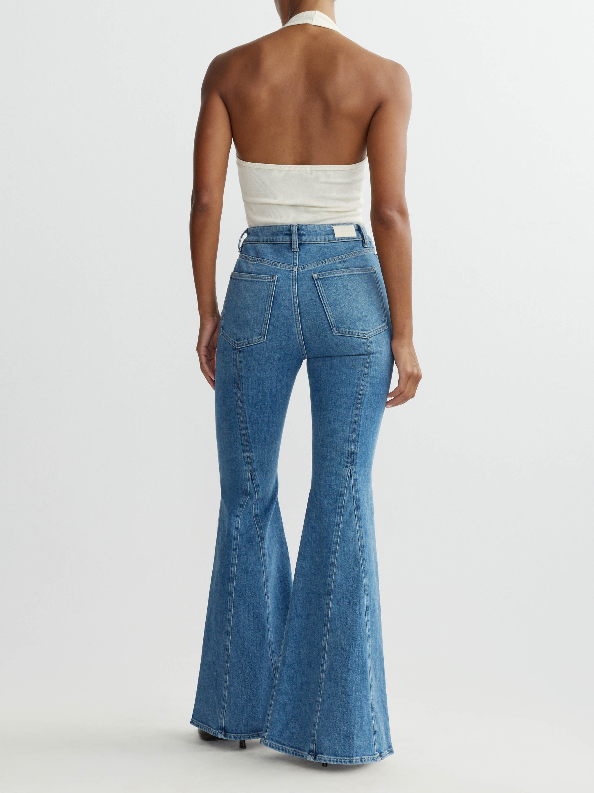 Person wearing blue flared jeans and a white top on a plain background