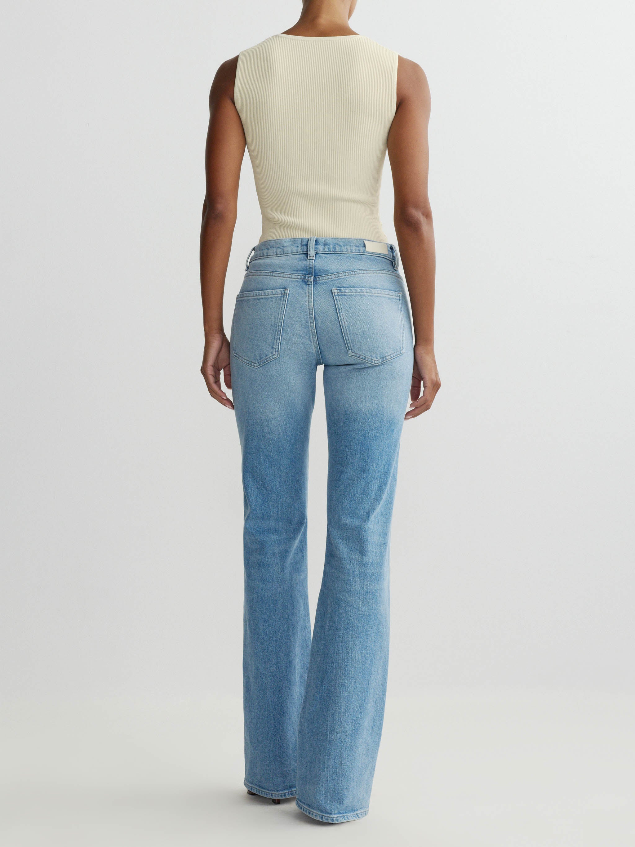 Person wearing a cream sleeveless top and light blue jeans on a white background