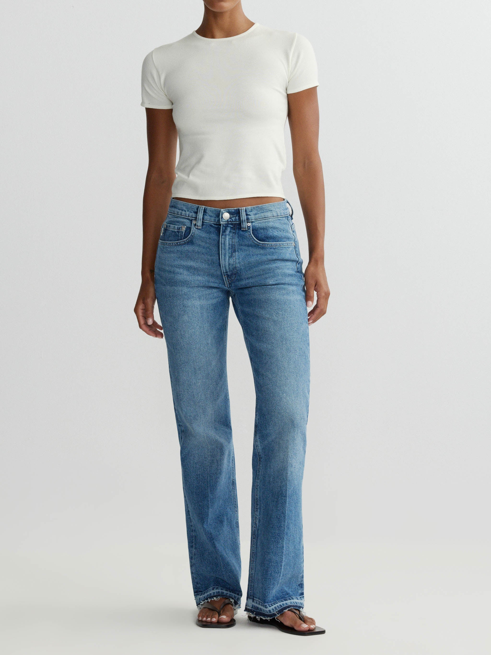 Person wearing a white t-shirt and blue jeans on a plain background