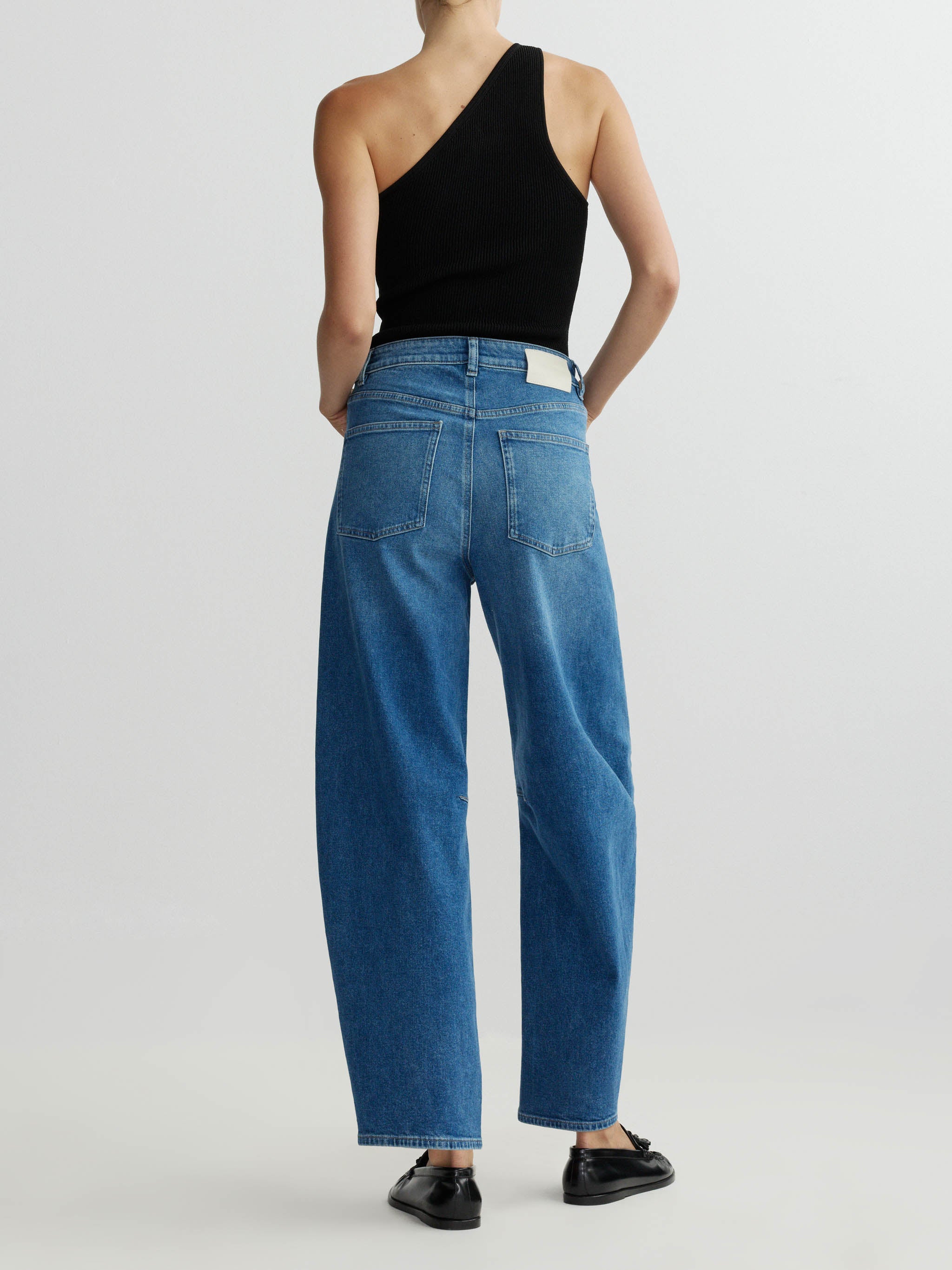 Person wearing blue jeans and a black one-shoulder top on a white background