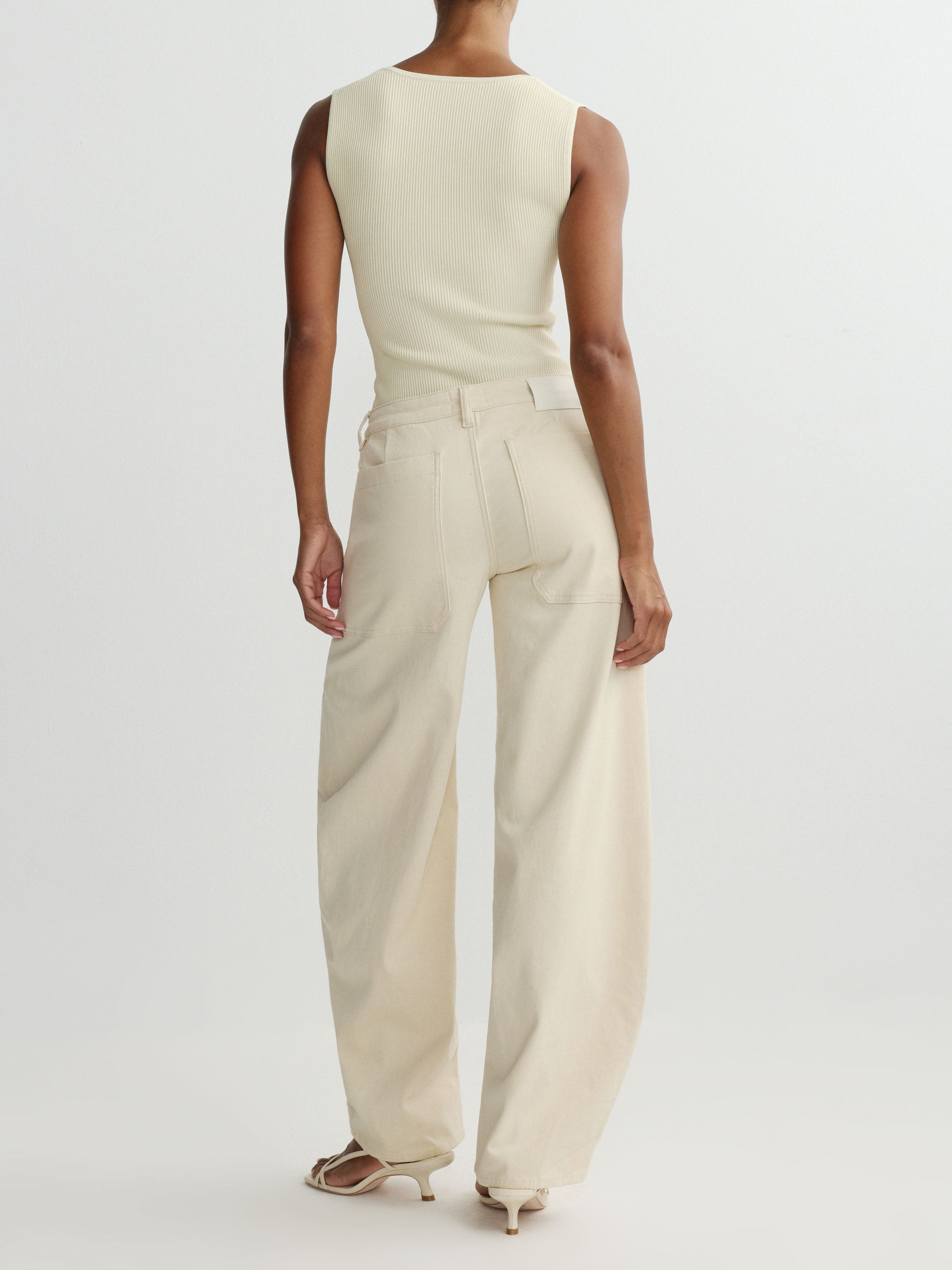 Person wearing a beige sleeveless top and wide-leg pants on a white background
