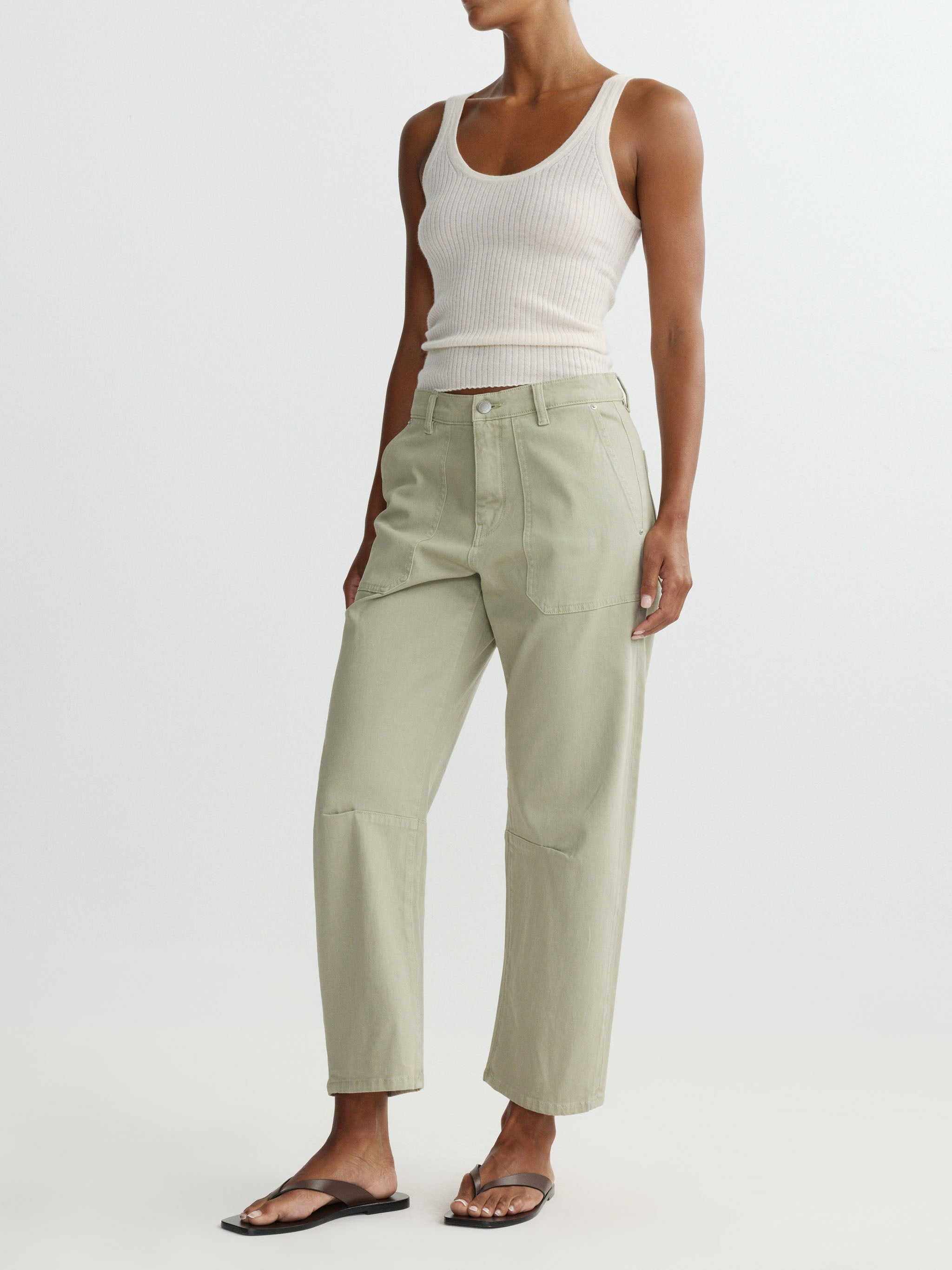 Person wearing a white tank top and light green pants on a plain background