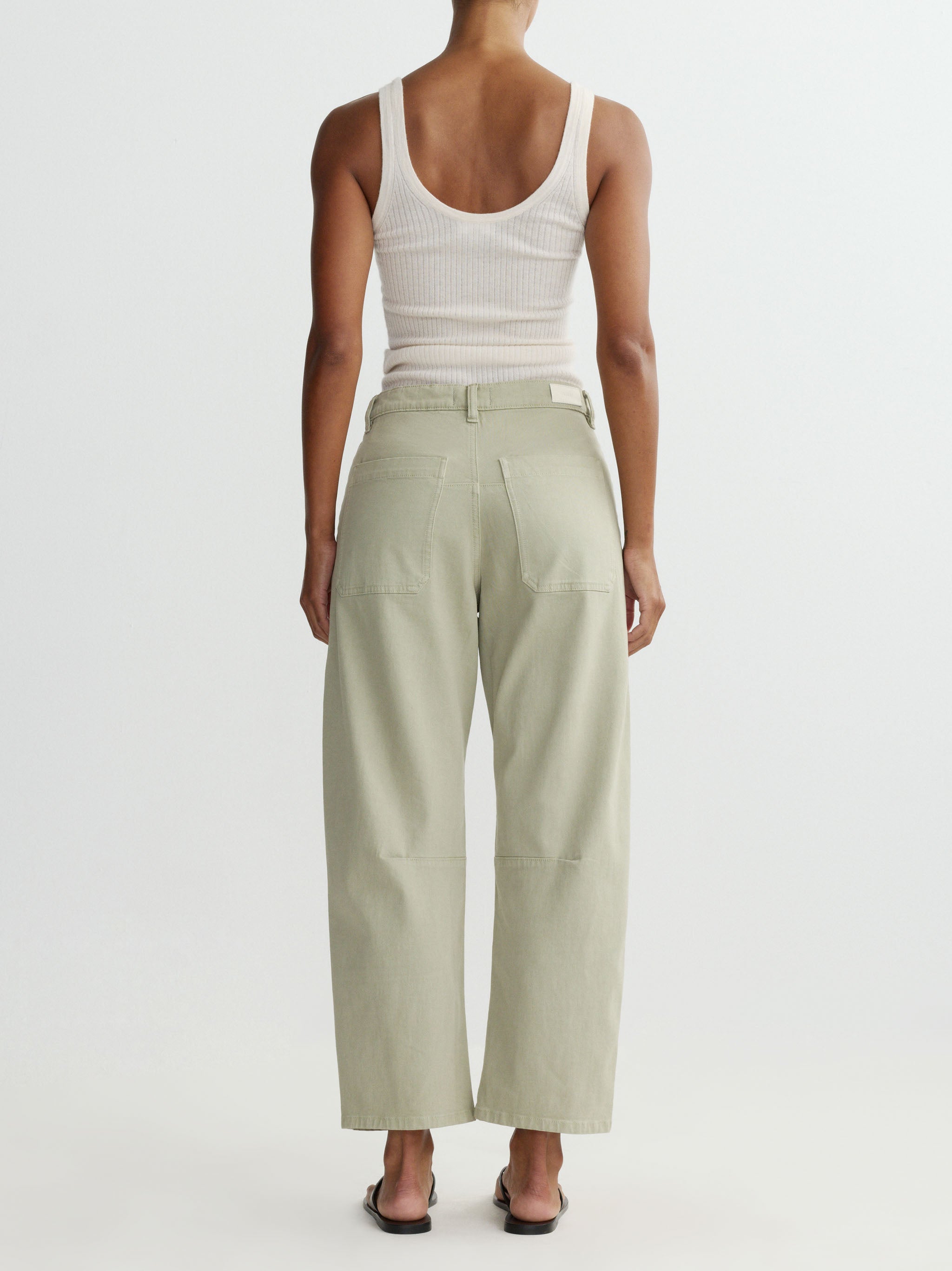 Person wearing a white tank top and light green pants on a white background