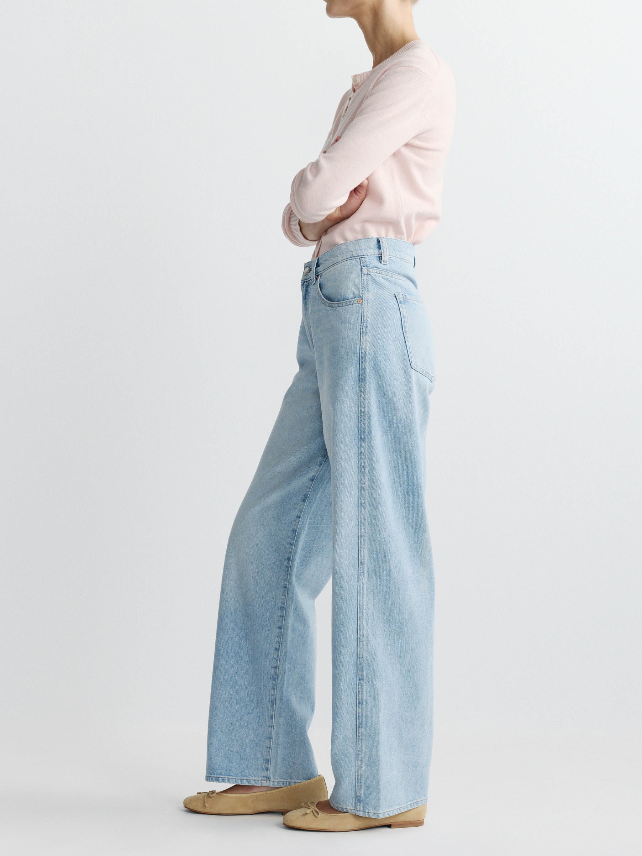 Person wearing light blue jeans and a pink shirt on a white background