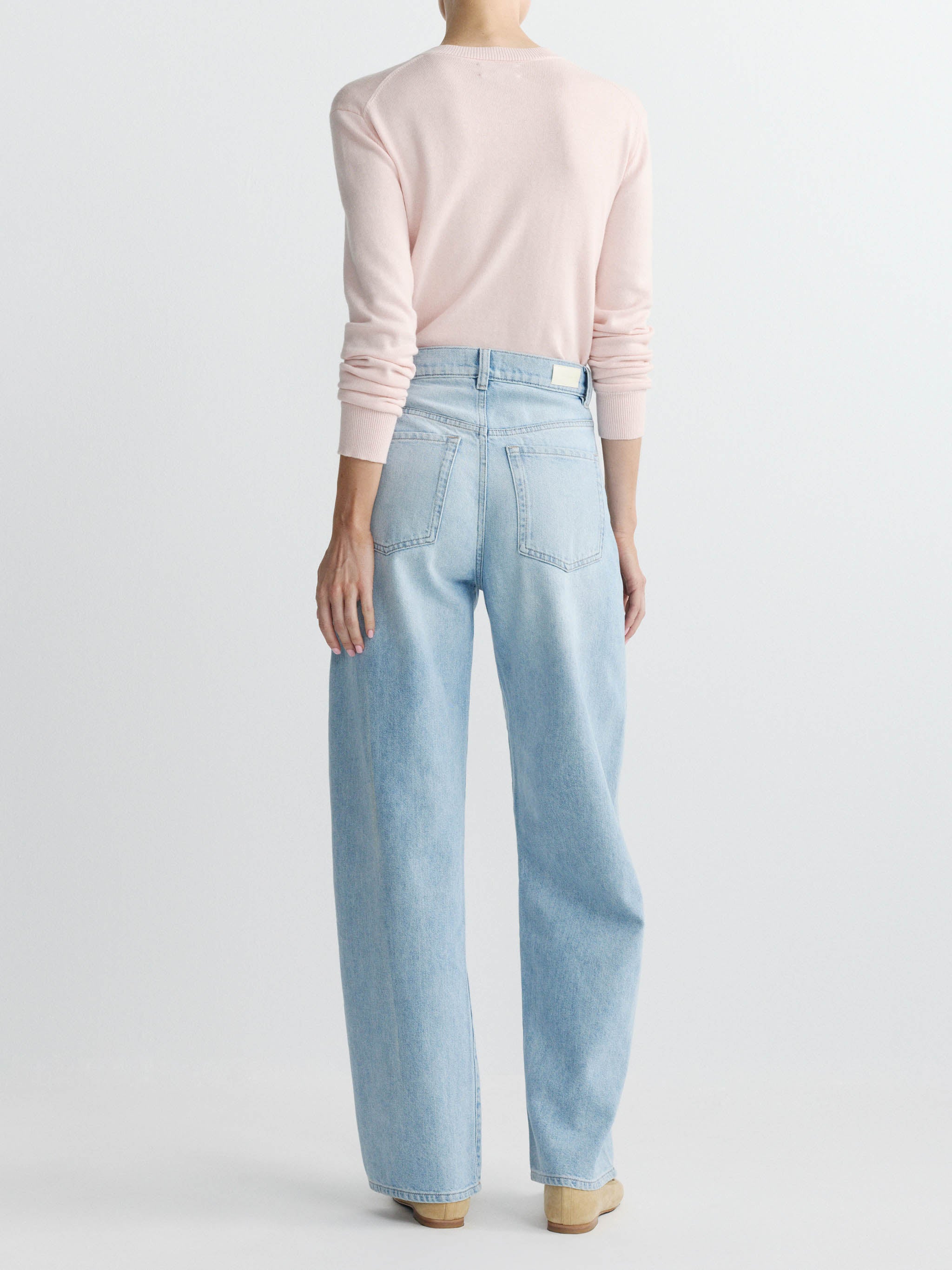 Person wearing light blue jeans and a pink sweater on a white background