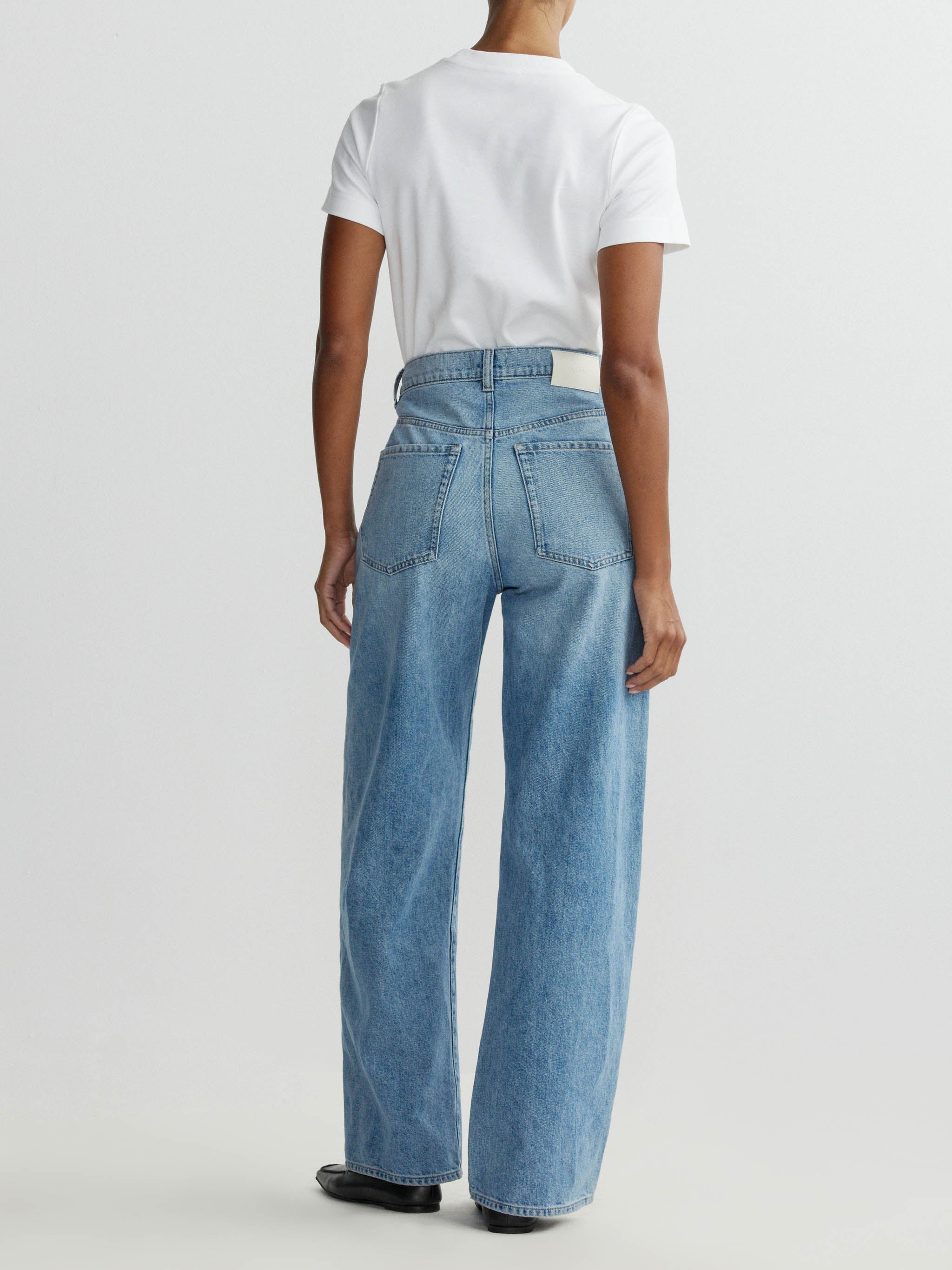Person wearing a white t-shirt and blue jeans on a plain background