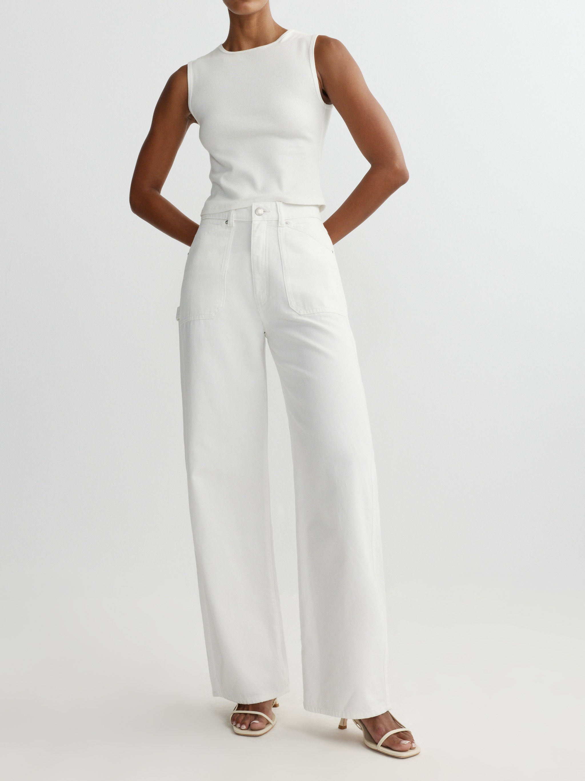 Person wearing a white sleeveless top and pants on a light gray background