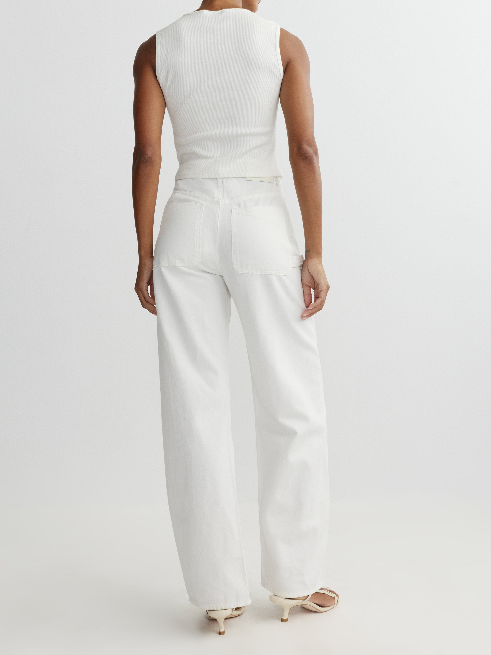 Person wearing a white sleeveless top and wide-leg pants on a light gray background