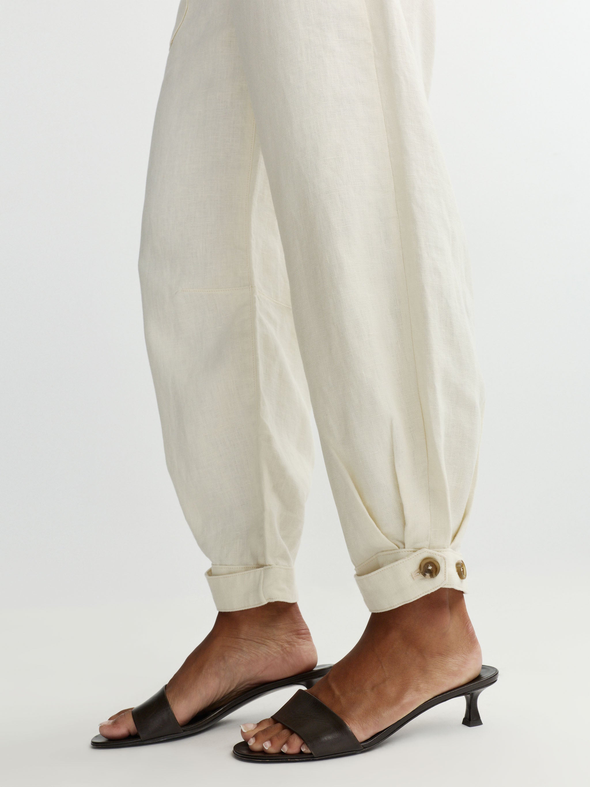 Person wearing white pants with hem button detail on a light gray background