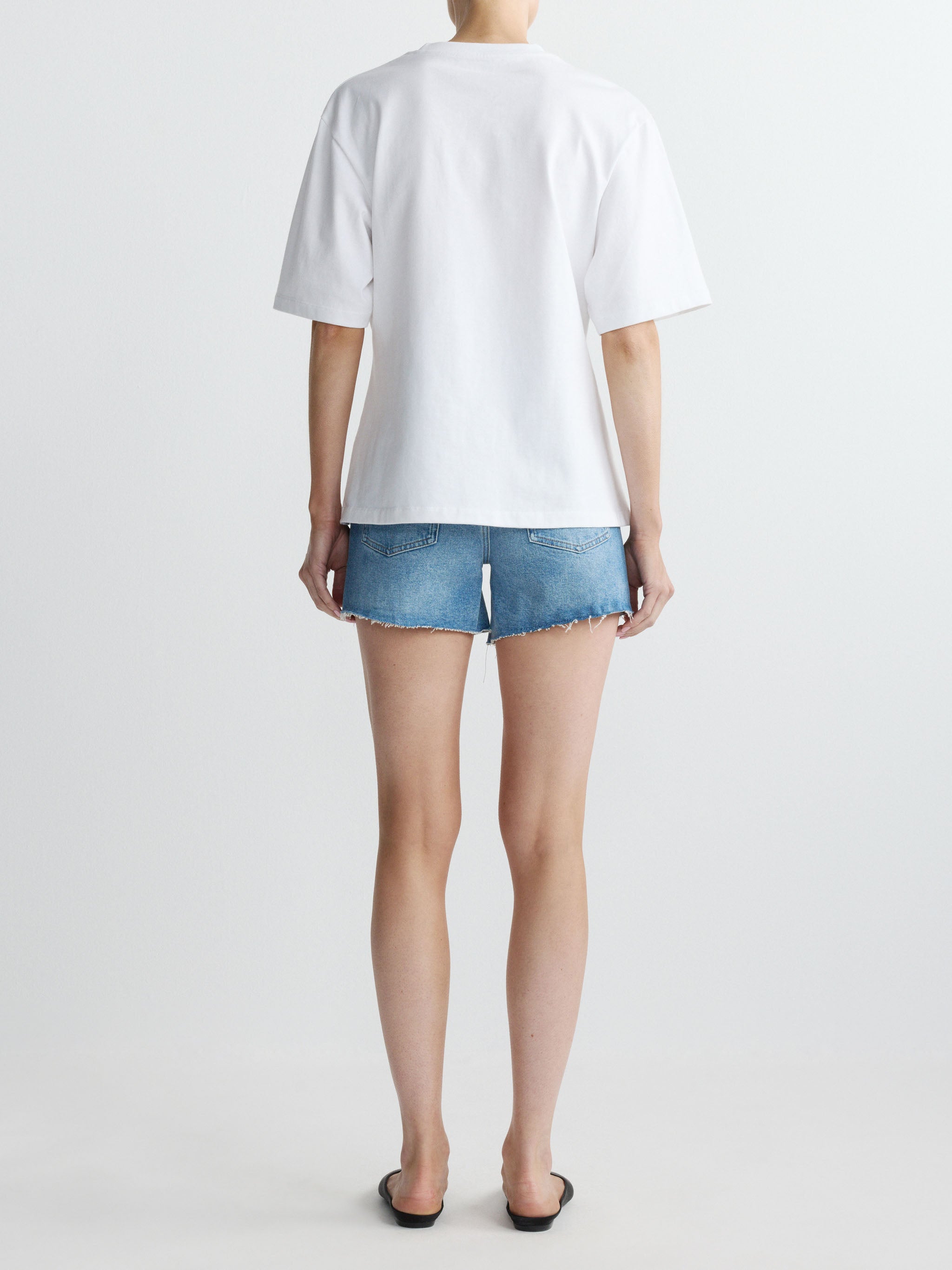 Person wearing a white t-shirt and denim shorts on a plain background