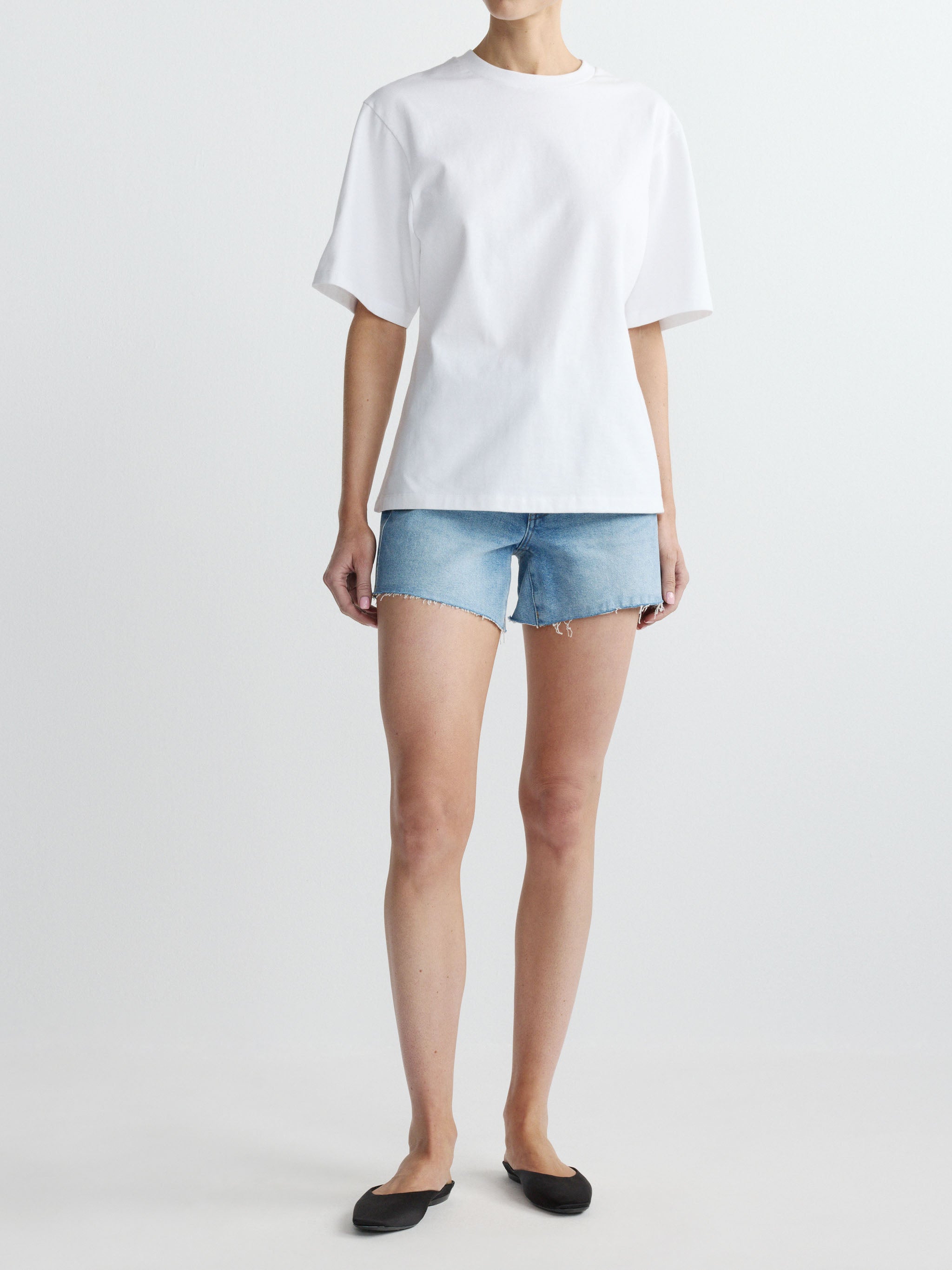 Person wearing a white t-shirt and denim shorts on a plain background
