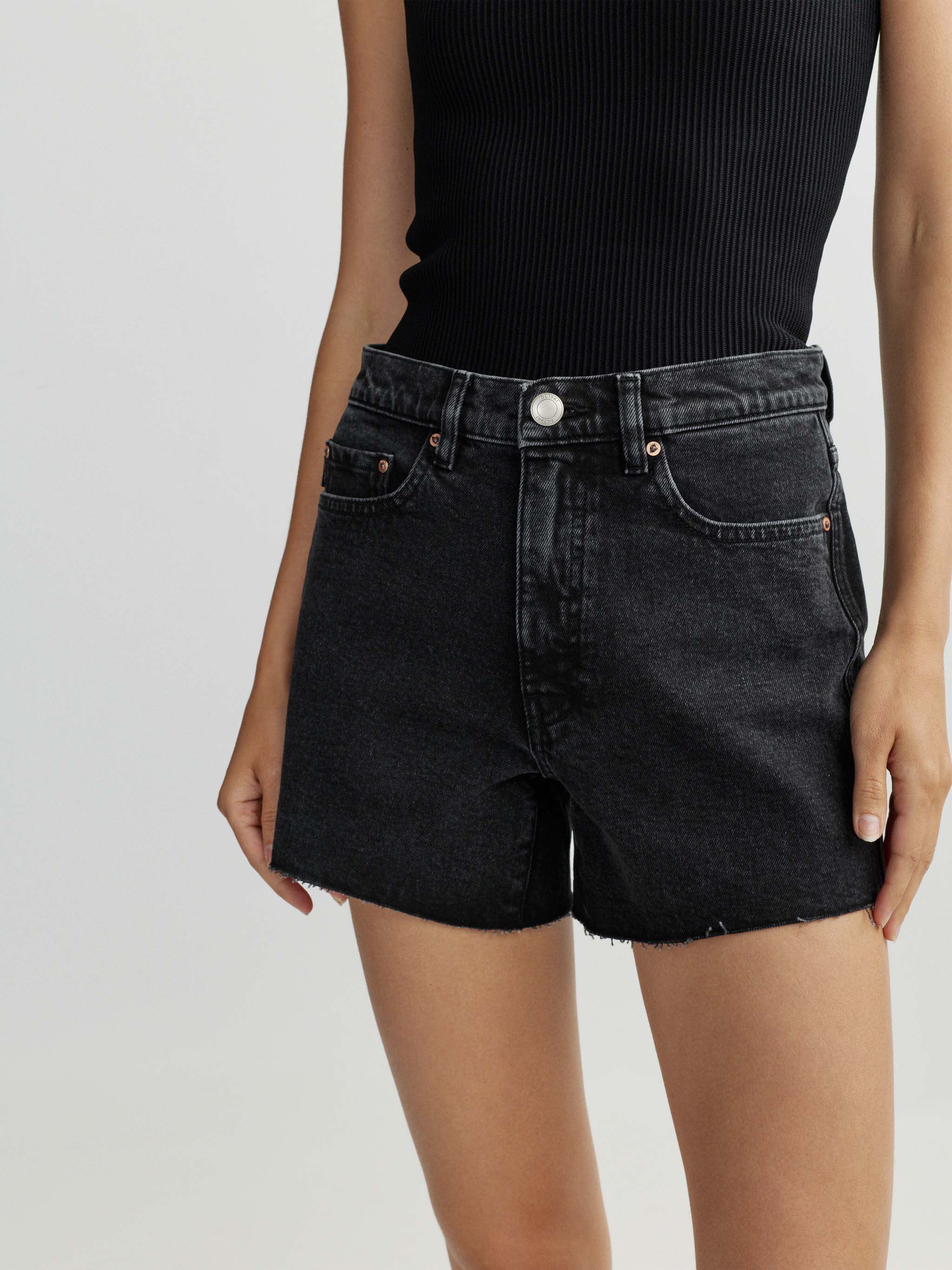 Person wearing black denim shorts and a black top on a light gray background