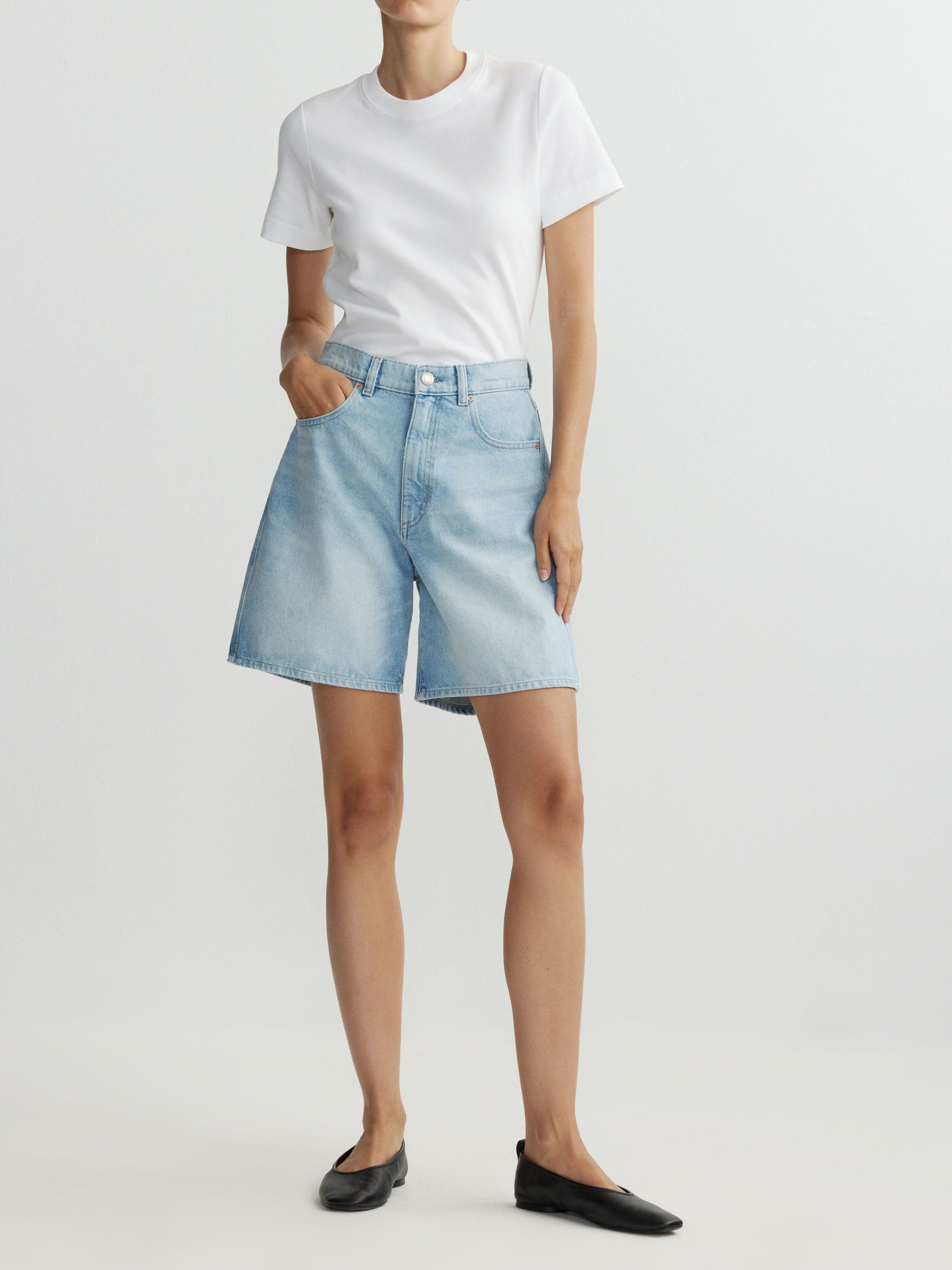 Person wearing light blue denim shorts and a white t-shirt on a plain background