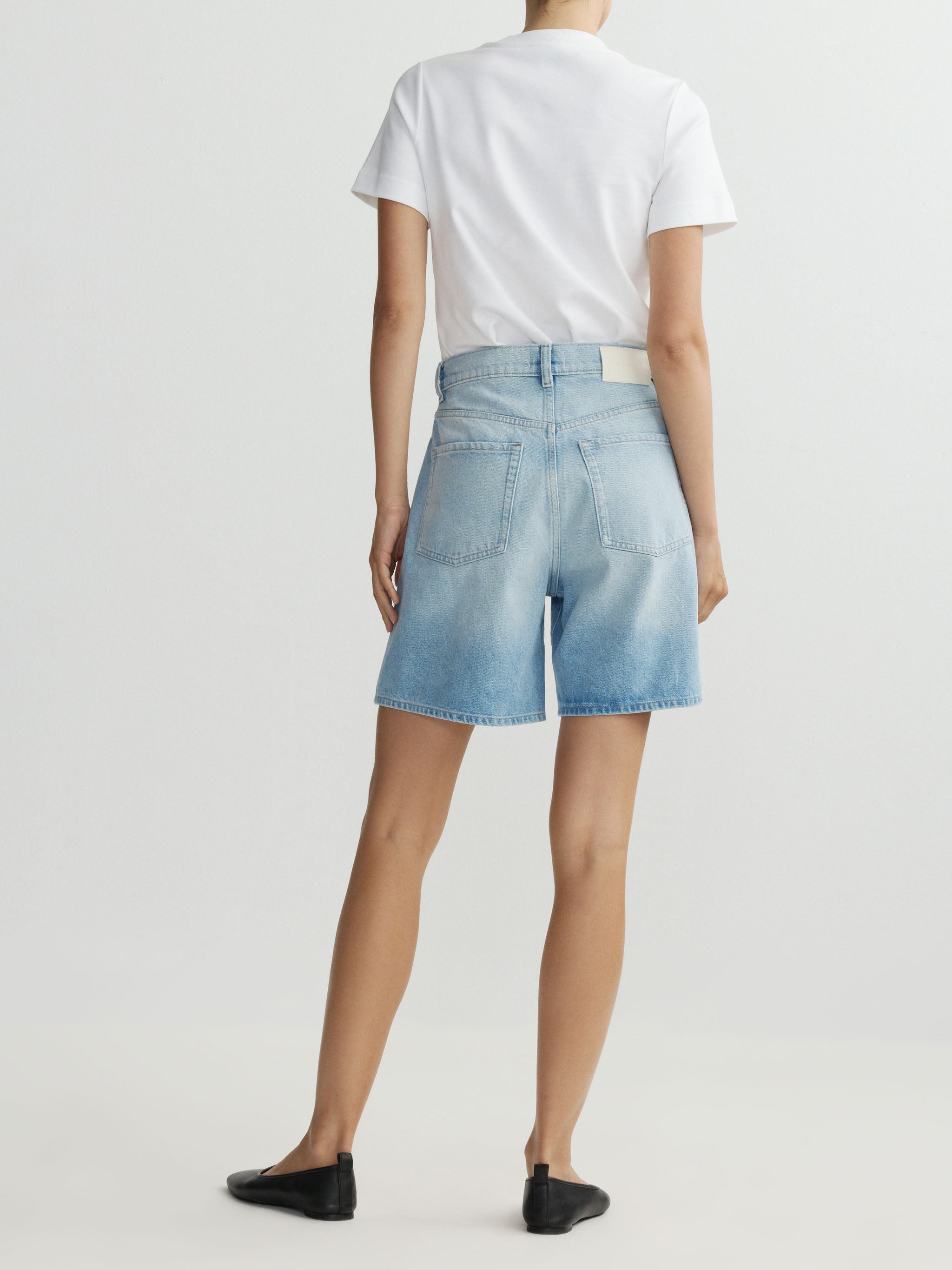 Person wearing light blue denim shorts and a white t-shirt on a plain background