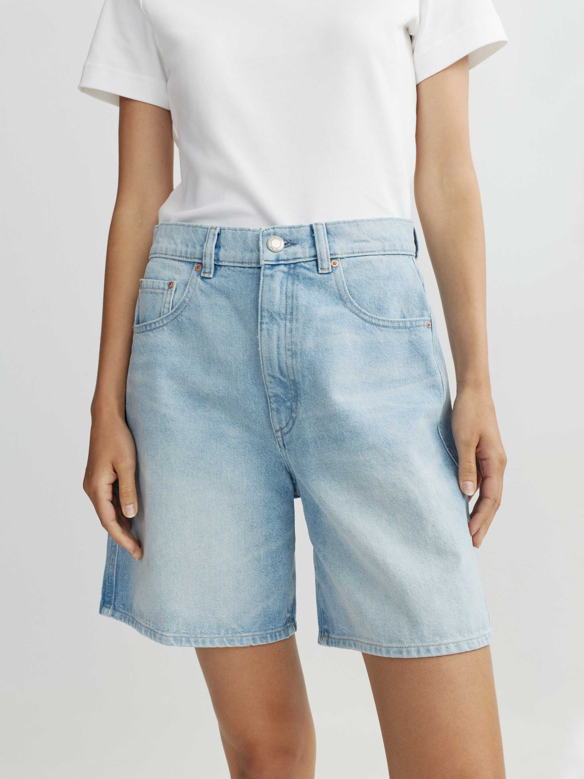Person wearing light blue denim shorts and a white t-shirt on a plain background
