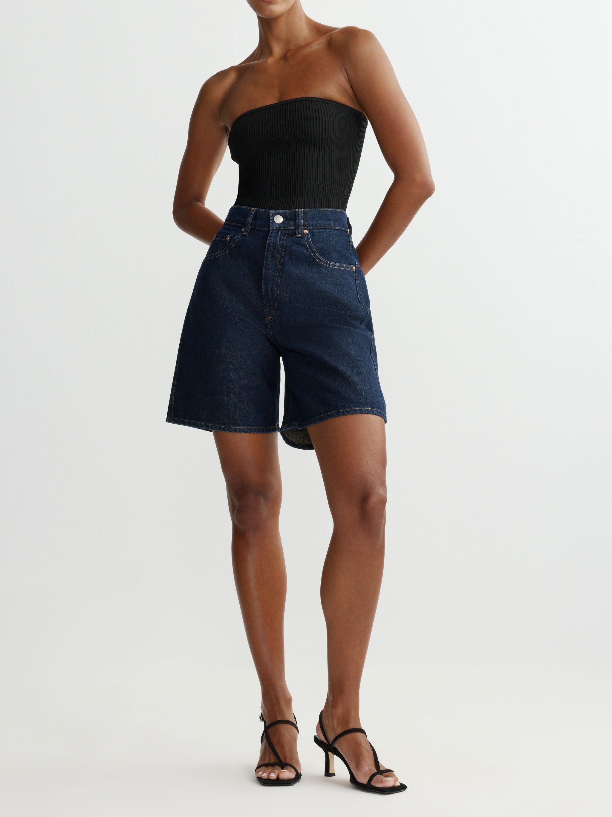 Person wearing a strapless black top and denim shorts on a white background