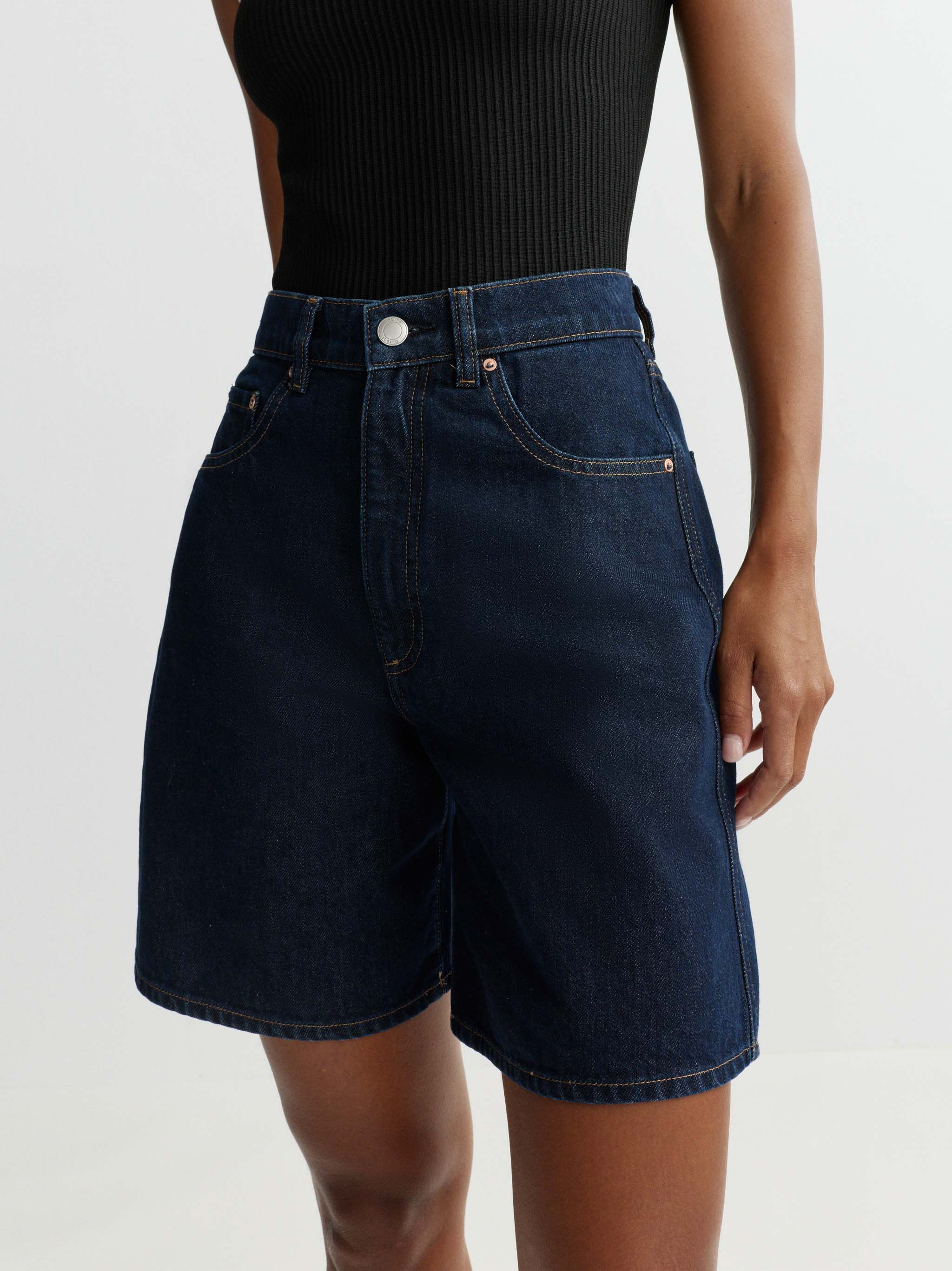 Person wearing dark blue denim shorts on a plain background