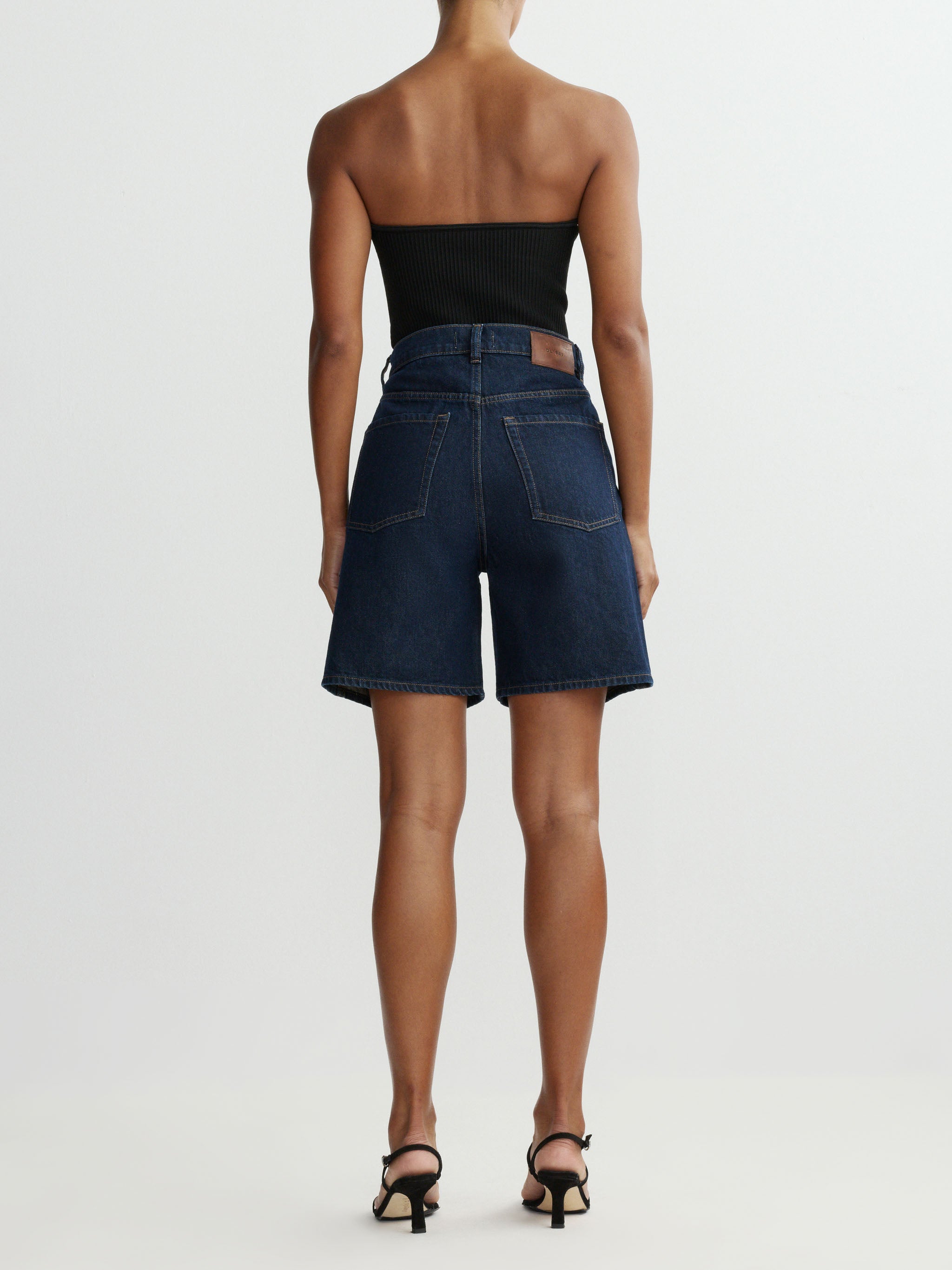 Person wearing a strapless black top and denim shorts on a white background