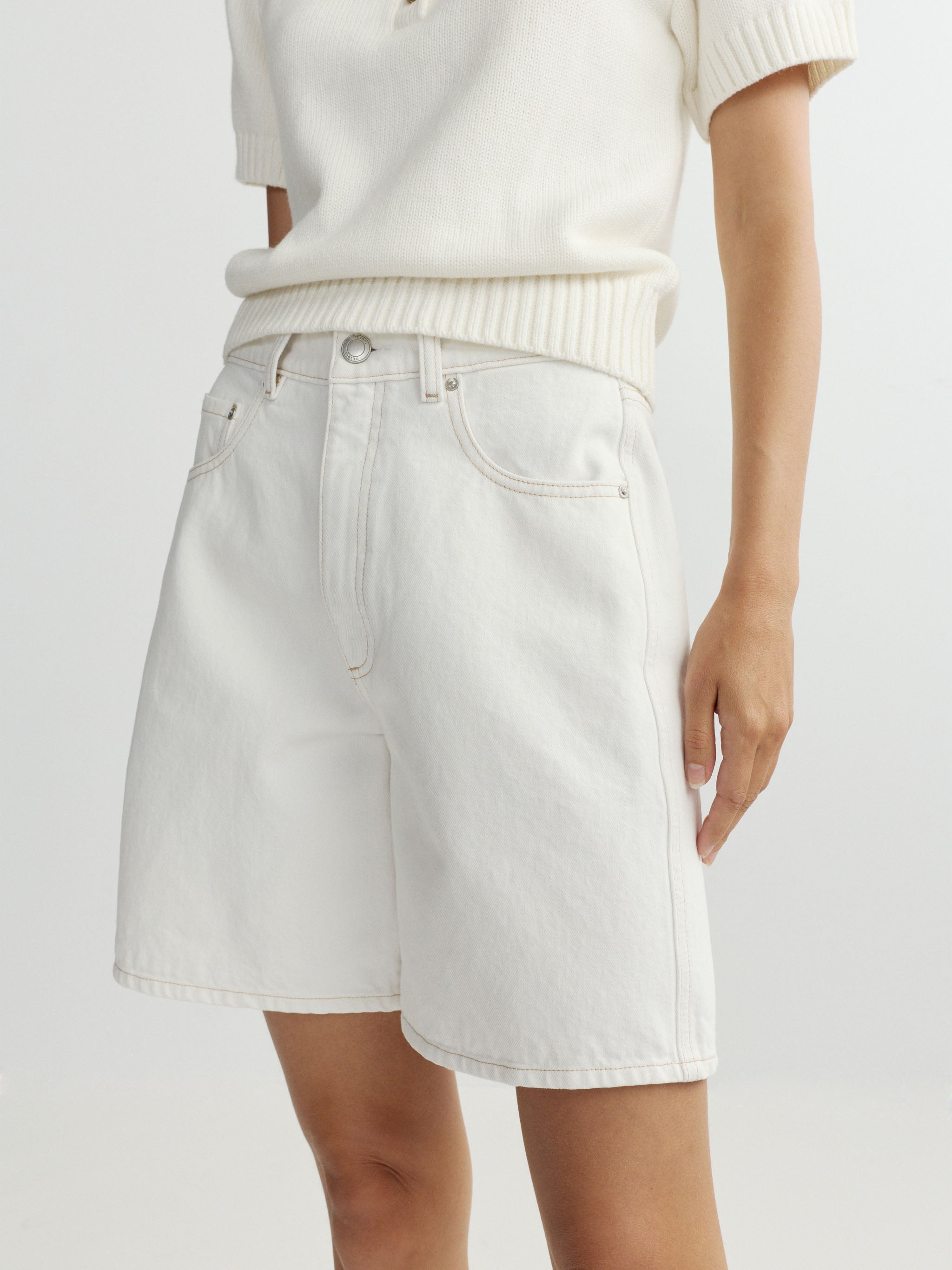 Person wearing a white polo shirt and white shorts on a light gray background