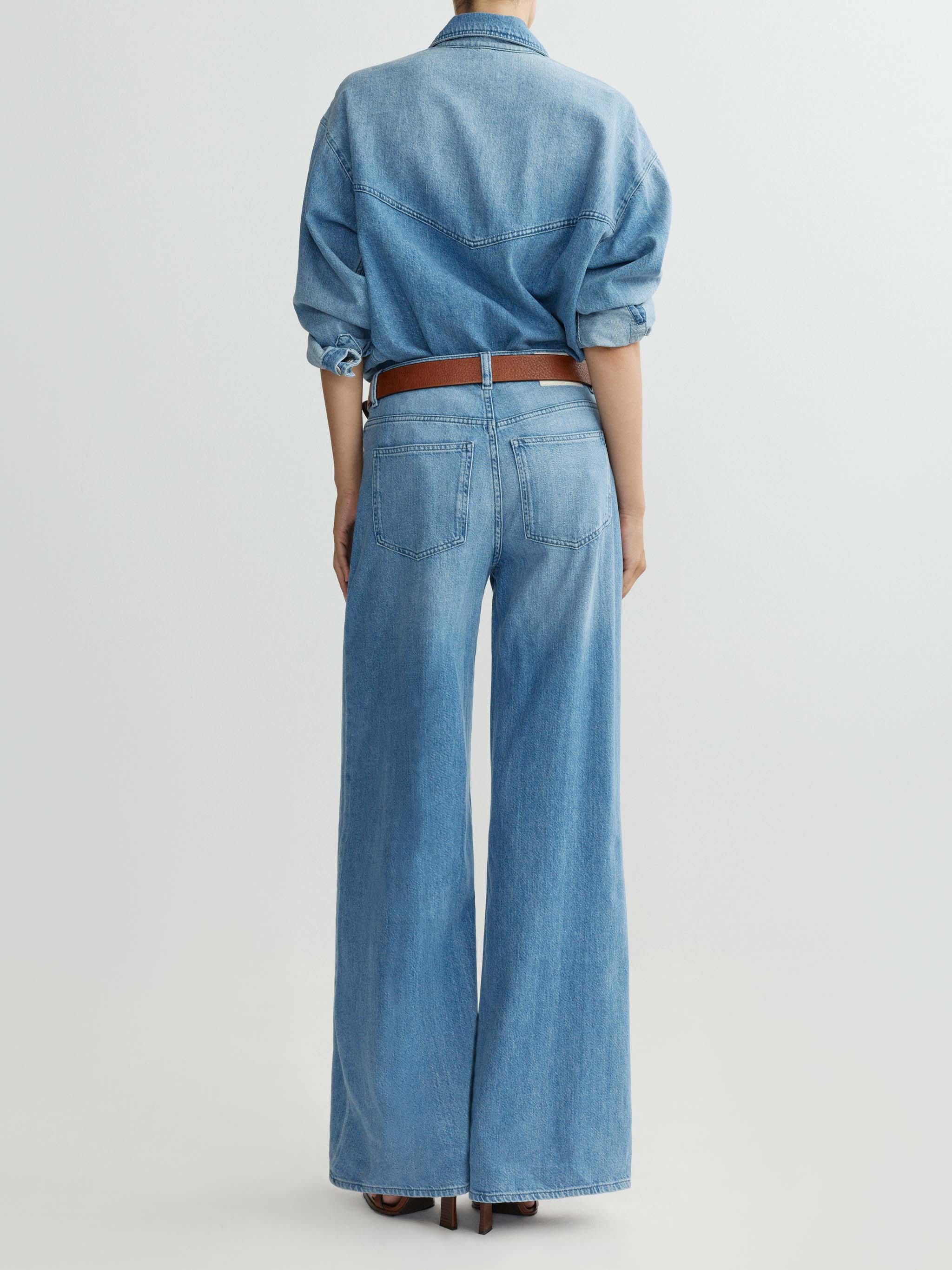 Person wearing a denim shirt and wide-leg jeans on a light gray background