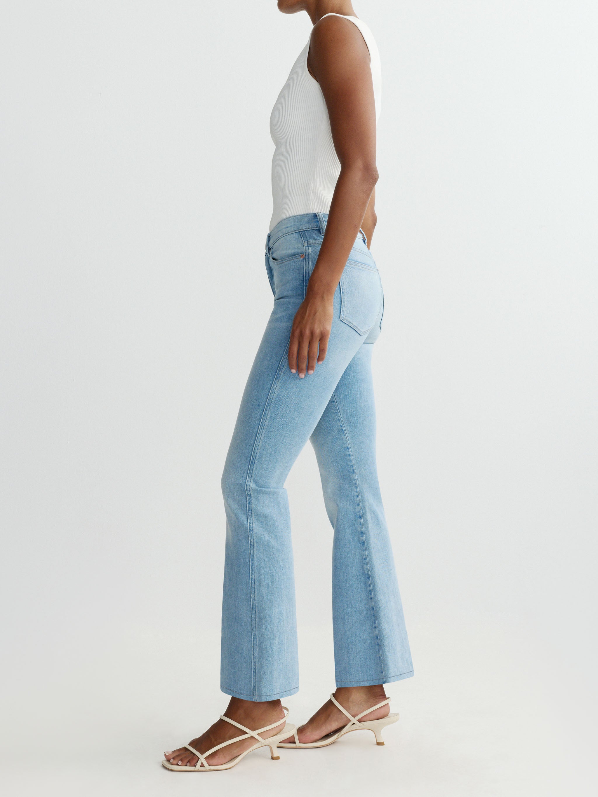 Person wearing light blue flared jeans on a white background