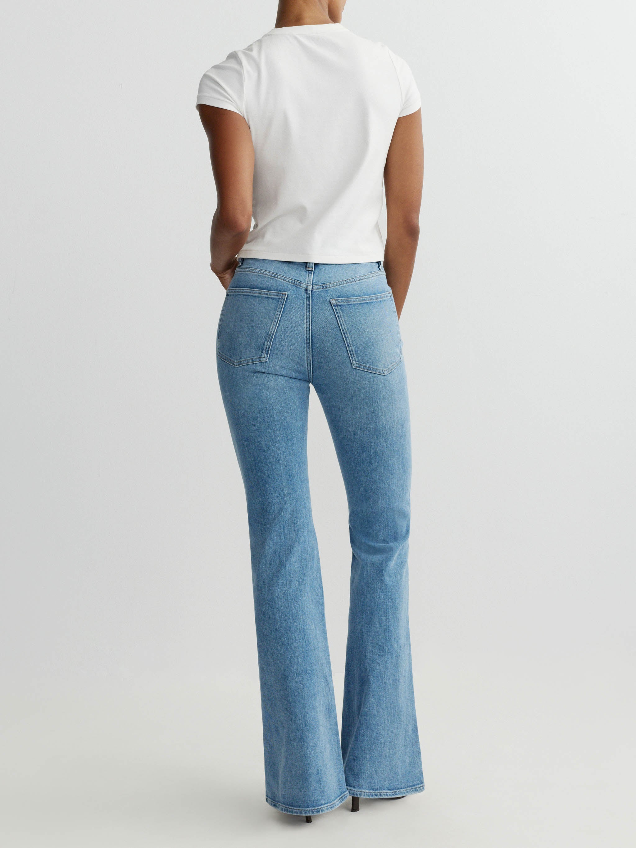 Person wearing blue flared jeans and a white top on a light gray background