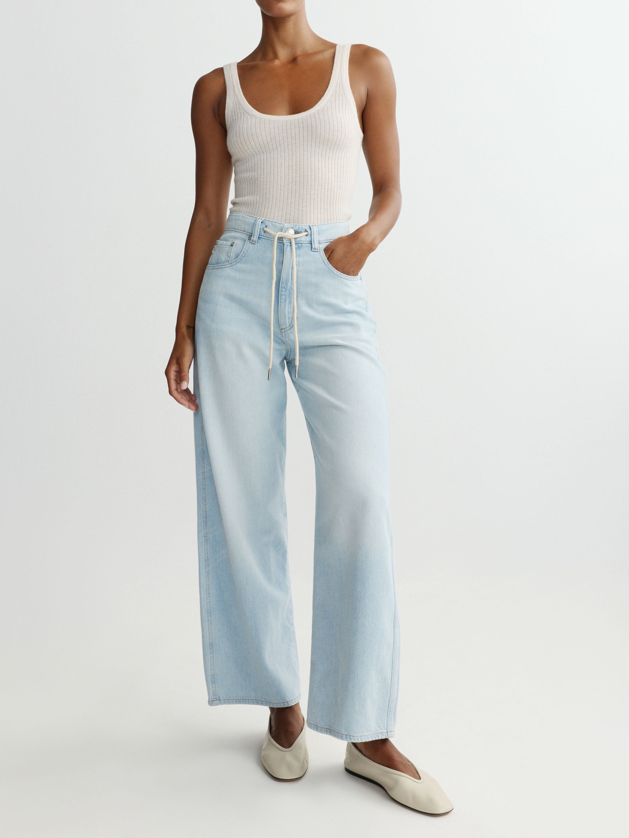Person wearing a white tank top and light blue jeans on a plain background
