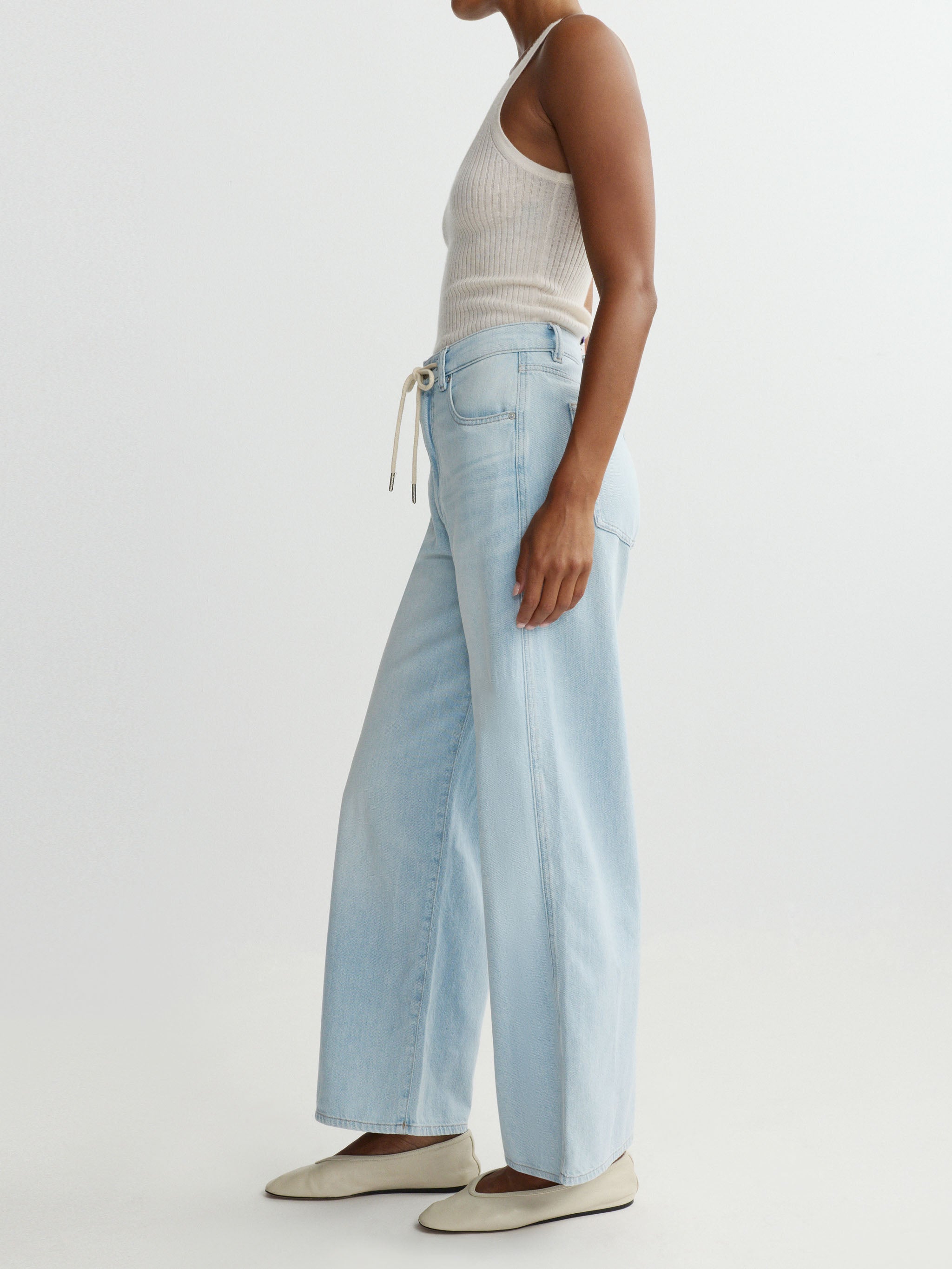 Person wearing light blue jeans and a white top on a plain background