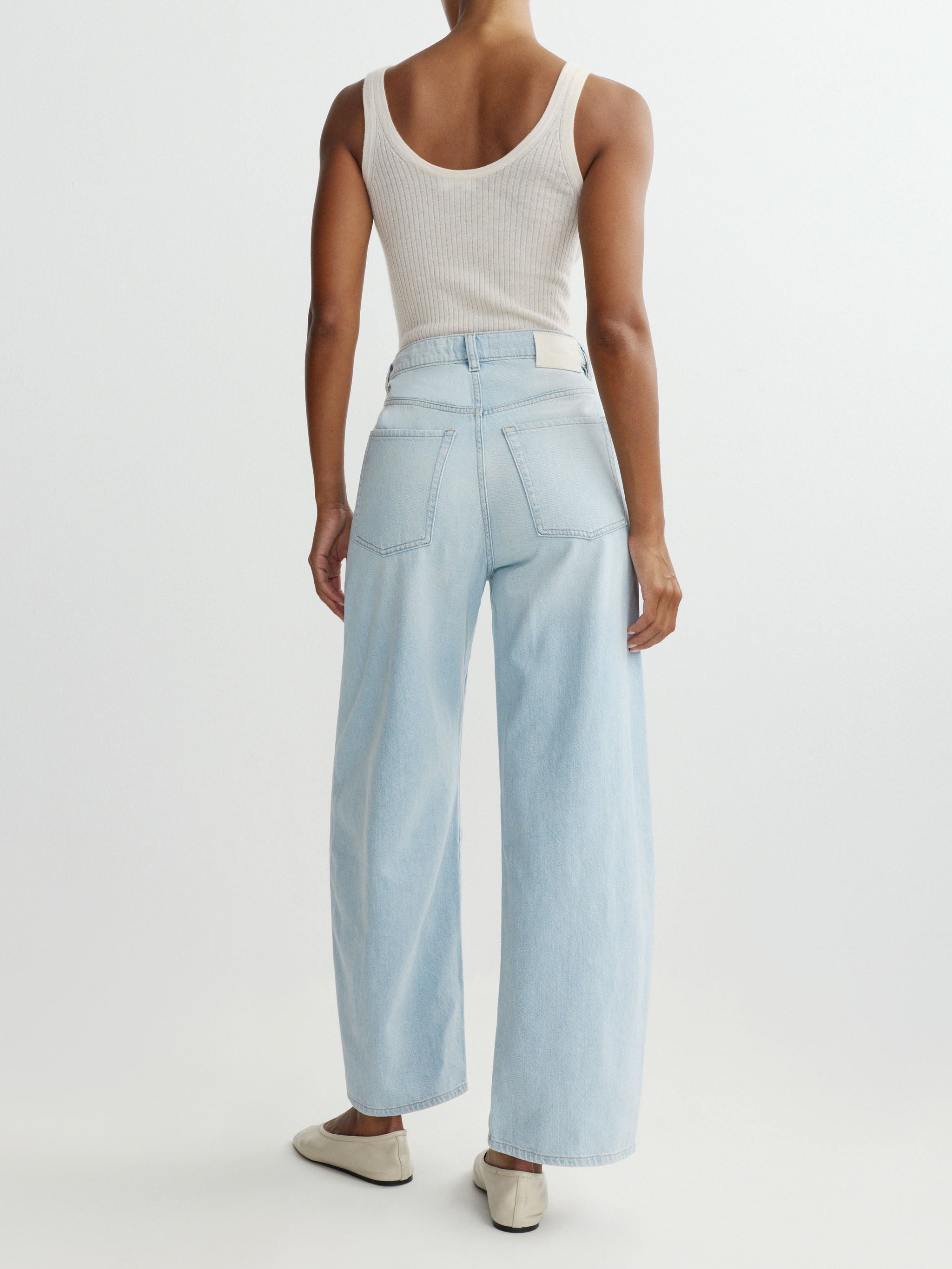Person wearing light blue wide-leg pants and a white tank top on a white background
