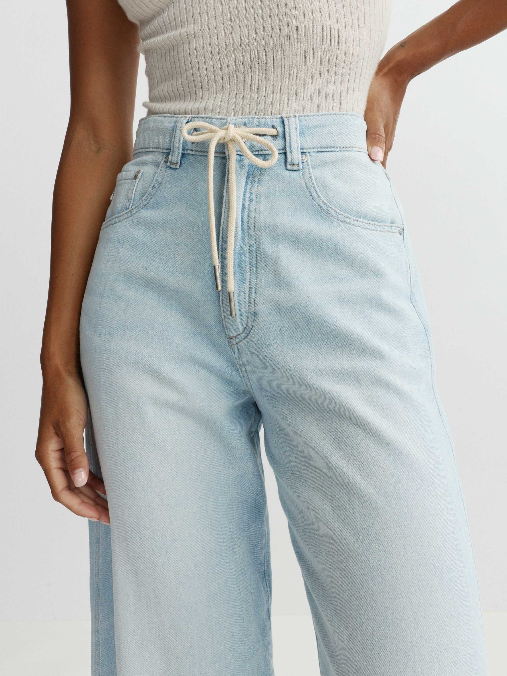Light blue jeans with a drawstring waist on a plain background