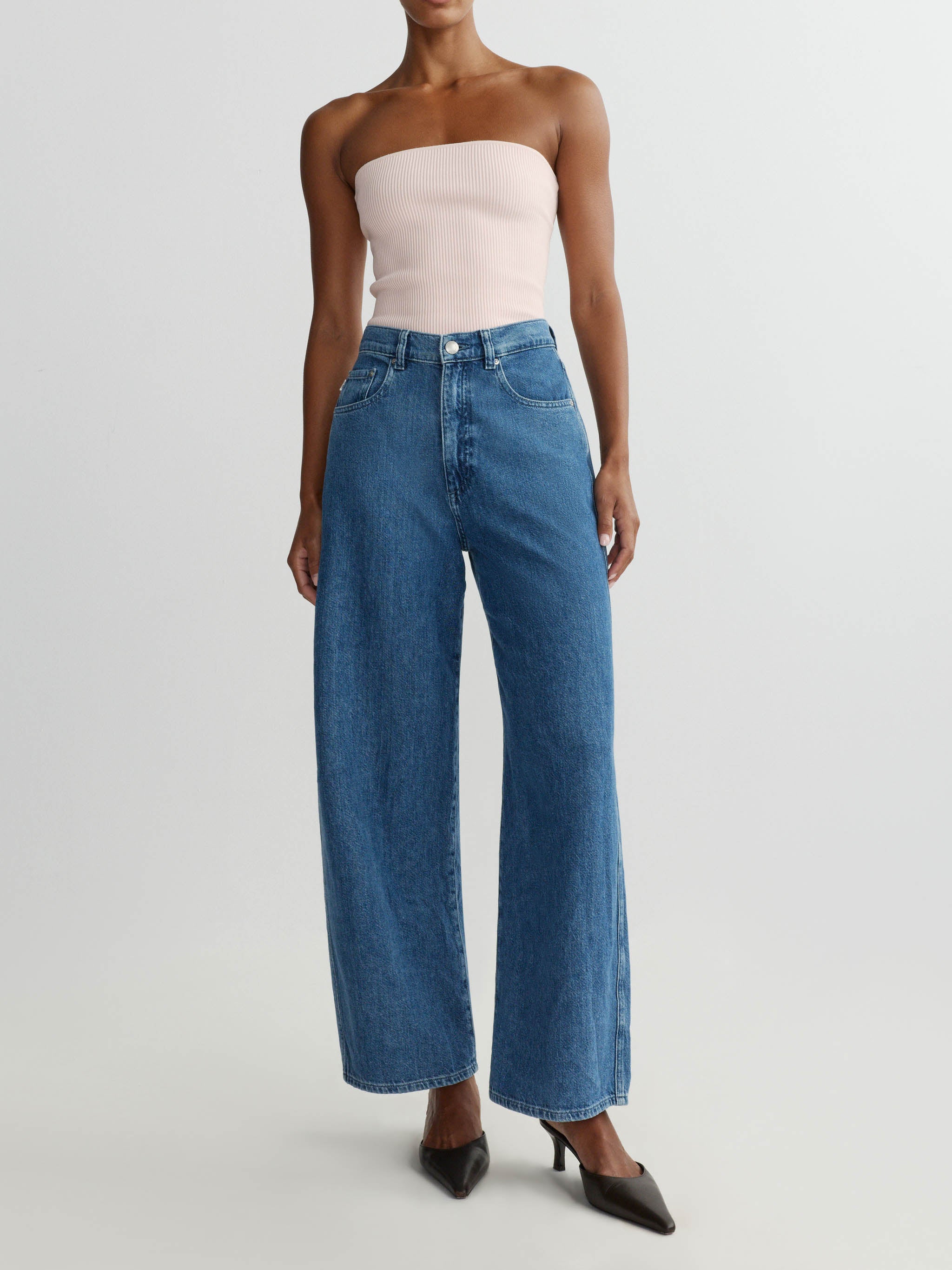 Woman wearing a strapless top and wide-leg jeans on a plain background